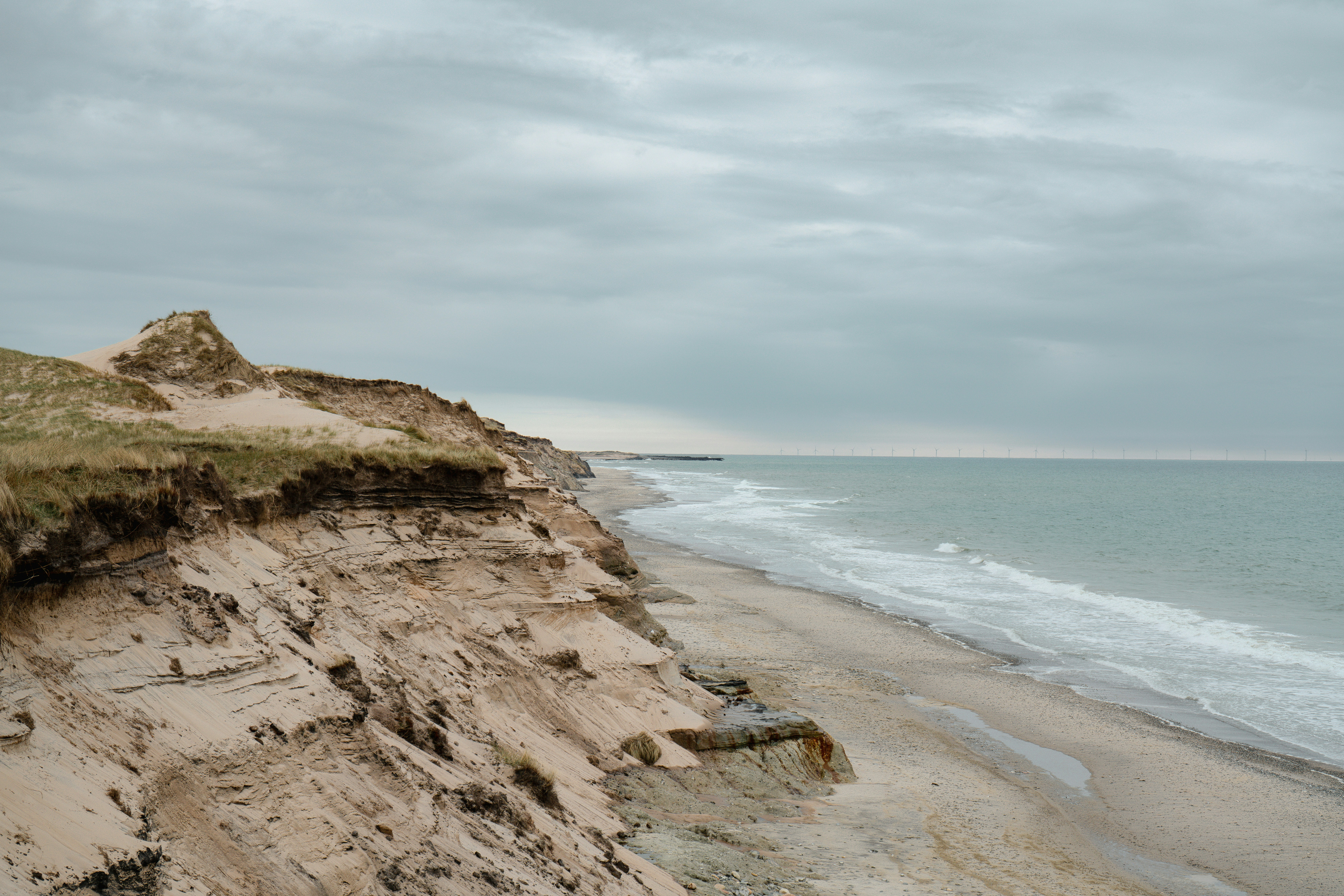 Sandy cliffs overlooking a beach with waves under a cloudy grey sky