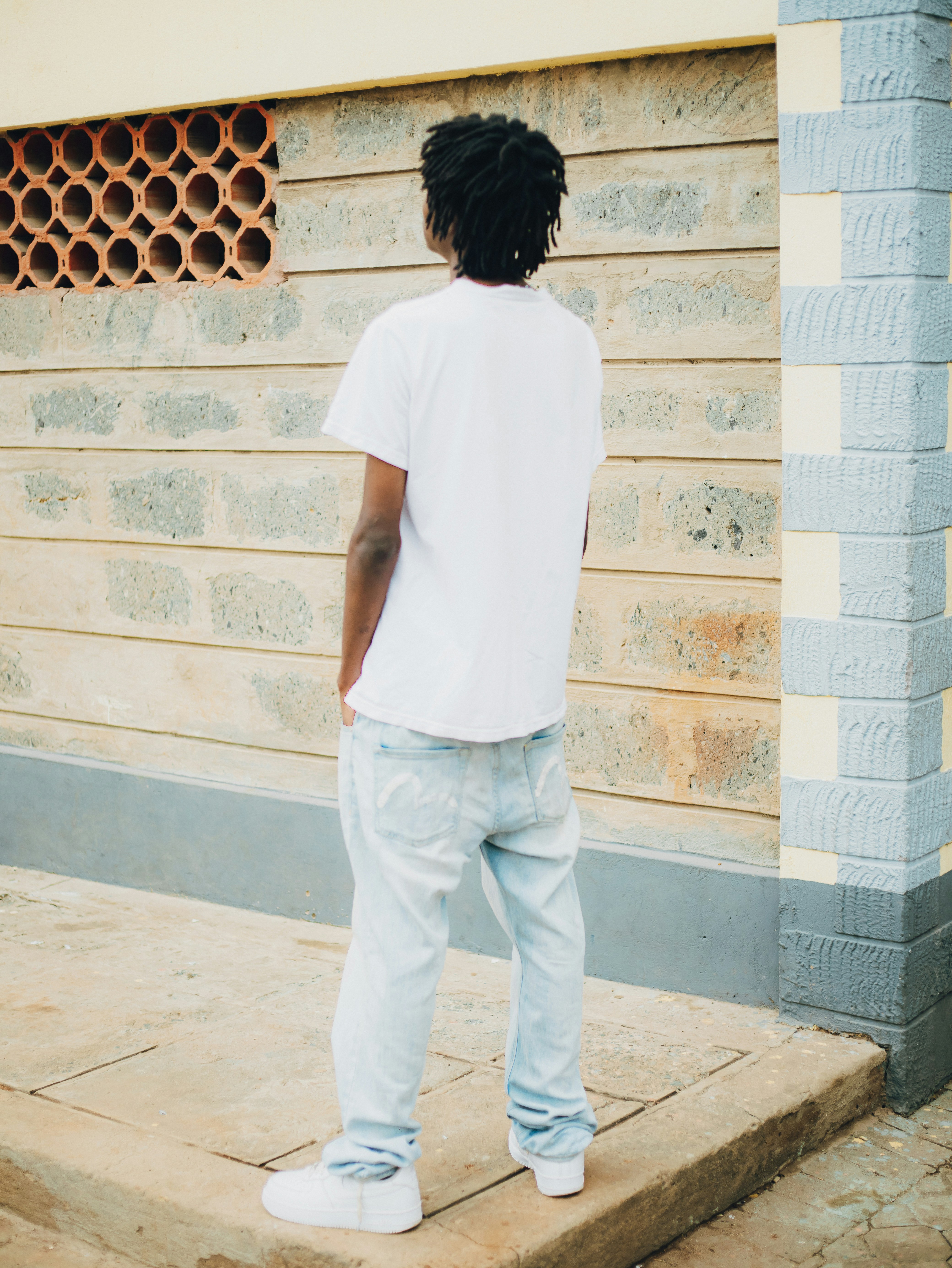 A person in a white t-shirt and light blue jeans against a stone wall