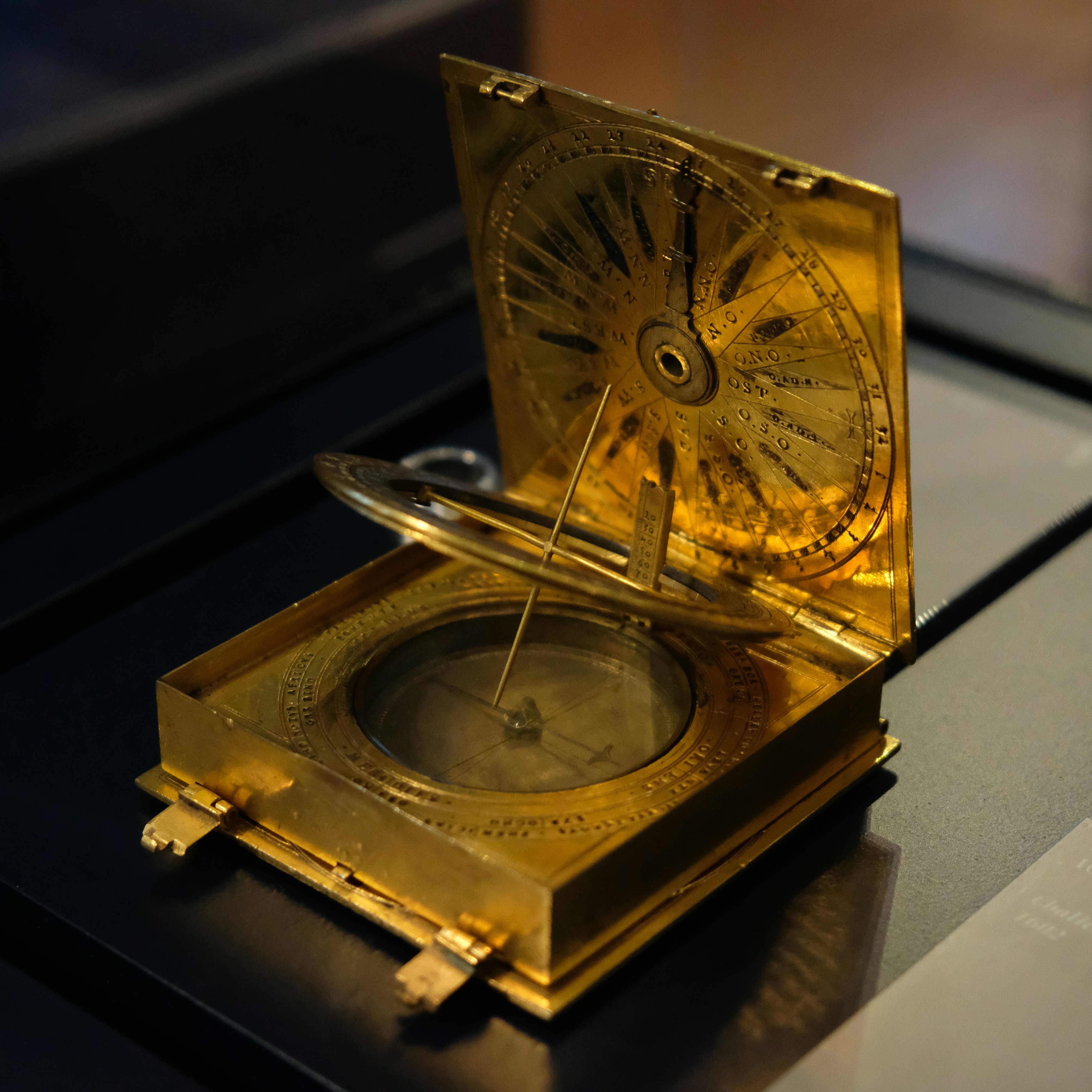 An antique brass sundial with a compass on a dark surface