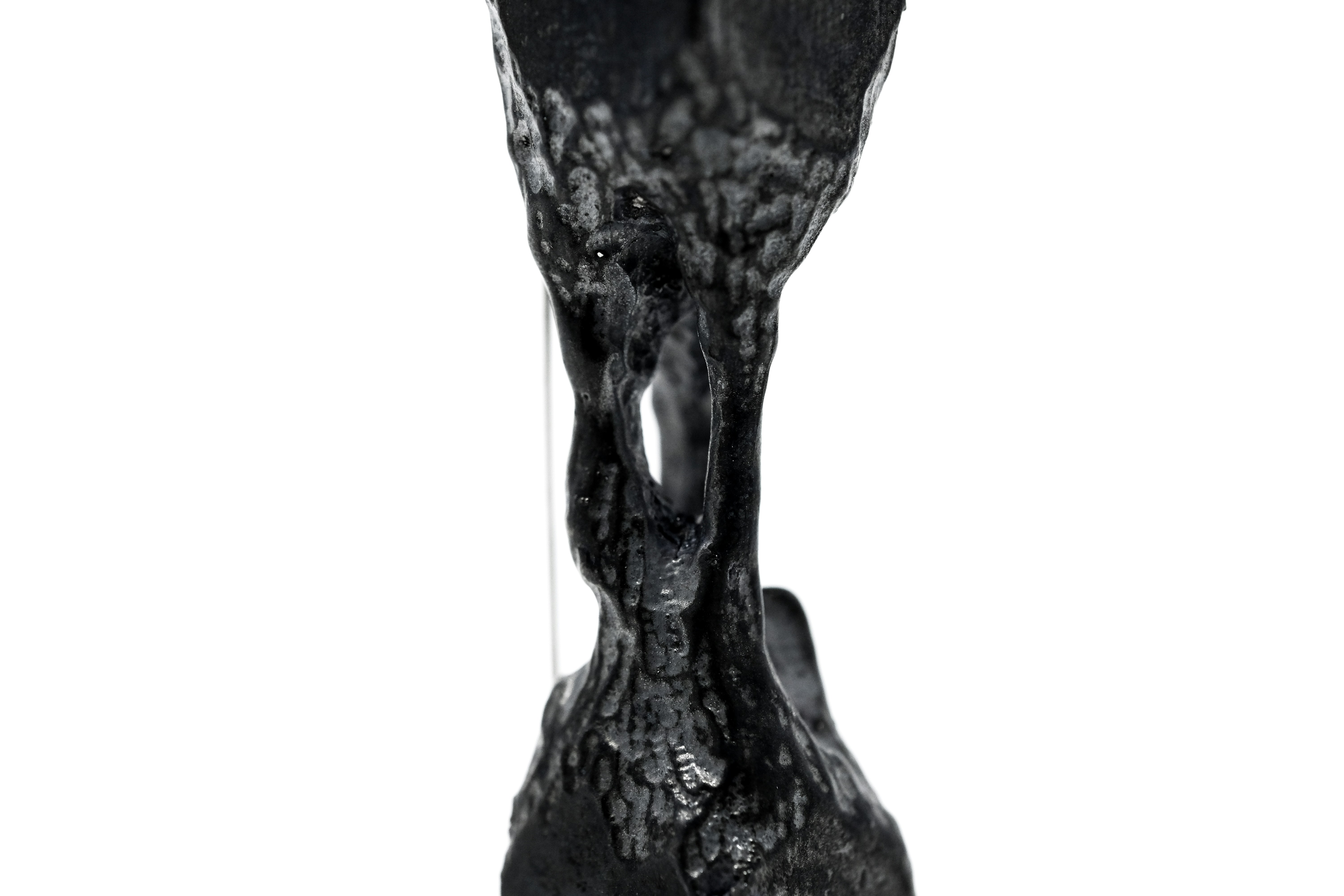 Una scultura verticale nera con un'apertura centrale su uno sfondo bianco