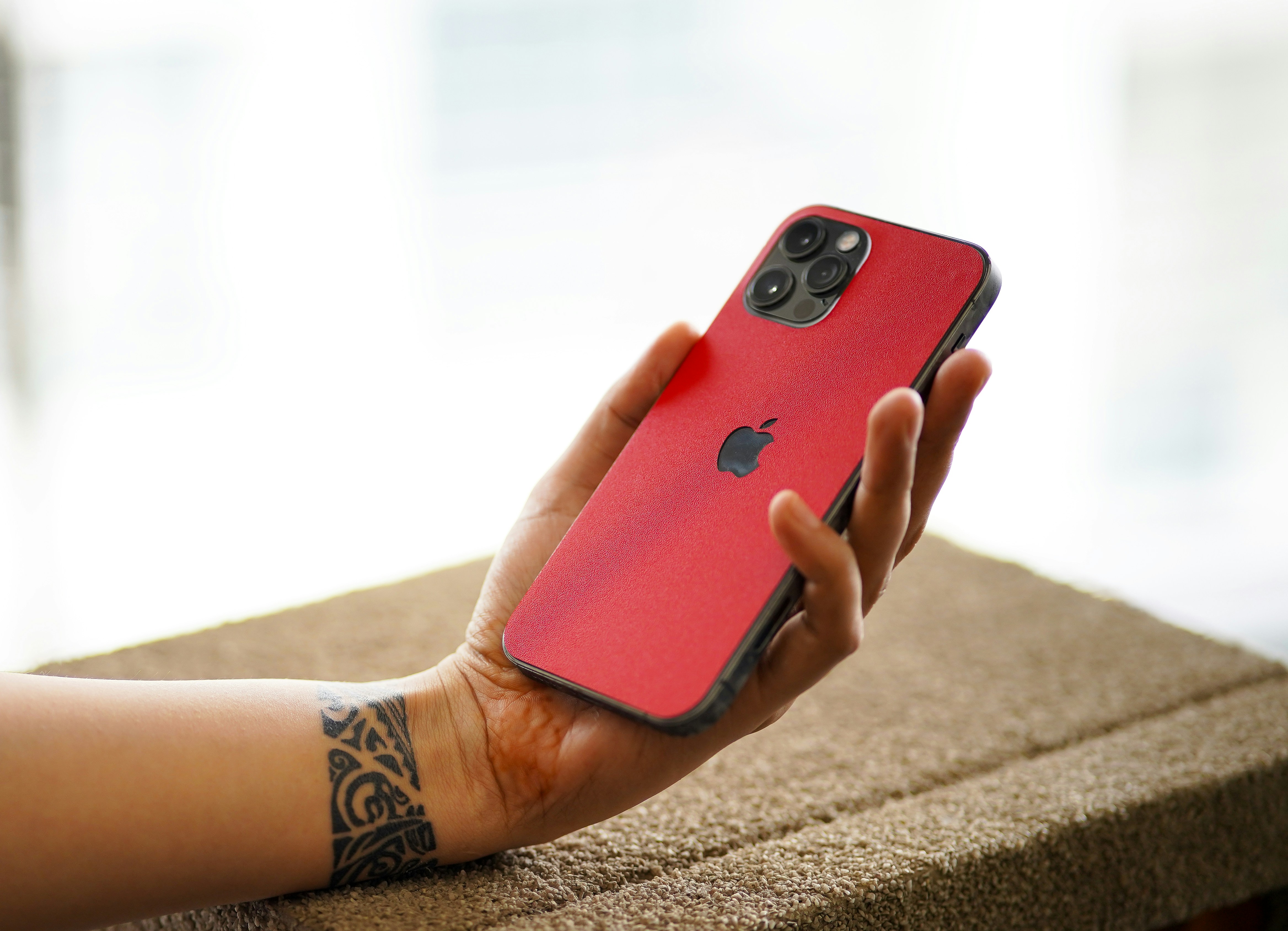 A person with a wrist tattoo holding a red smartphone in their hand
