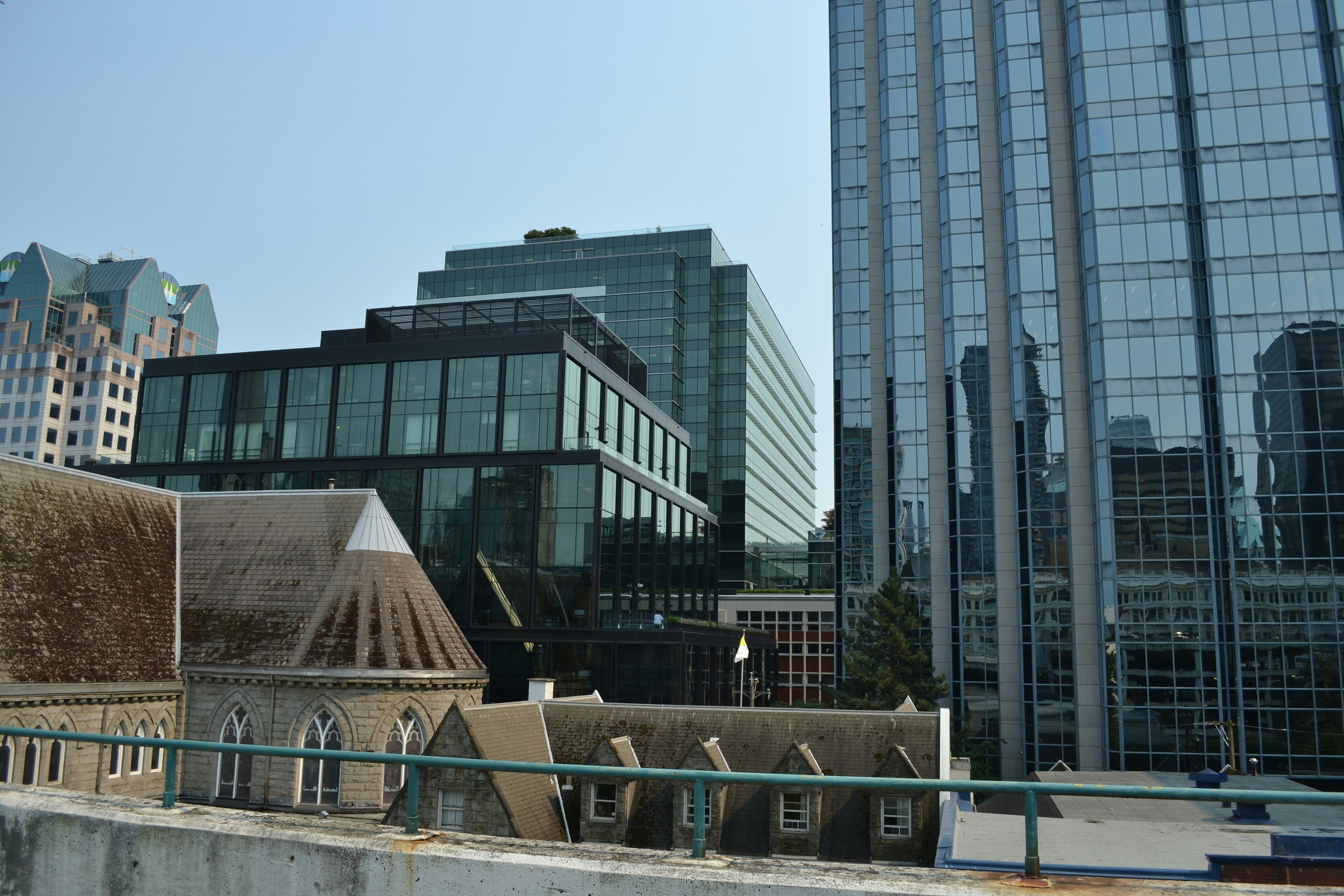 A stone church with a peaked roof beside modern glass skyscrapers in a city