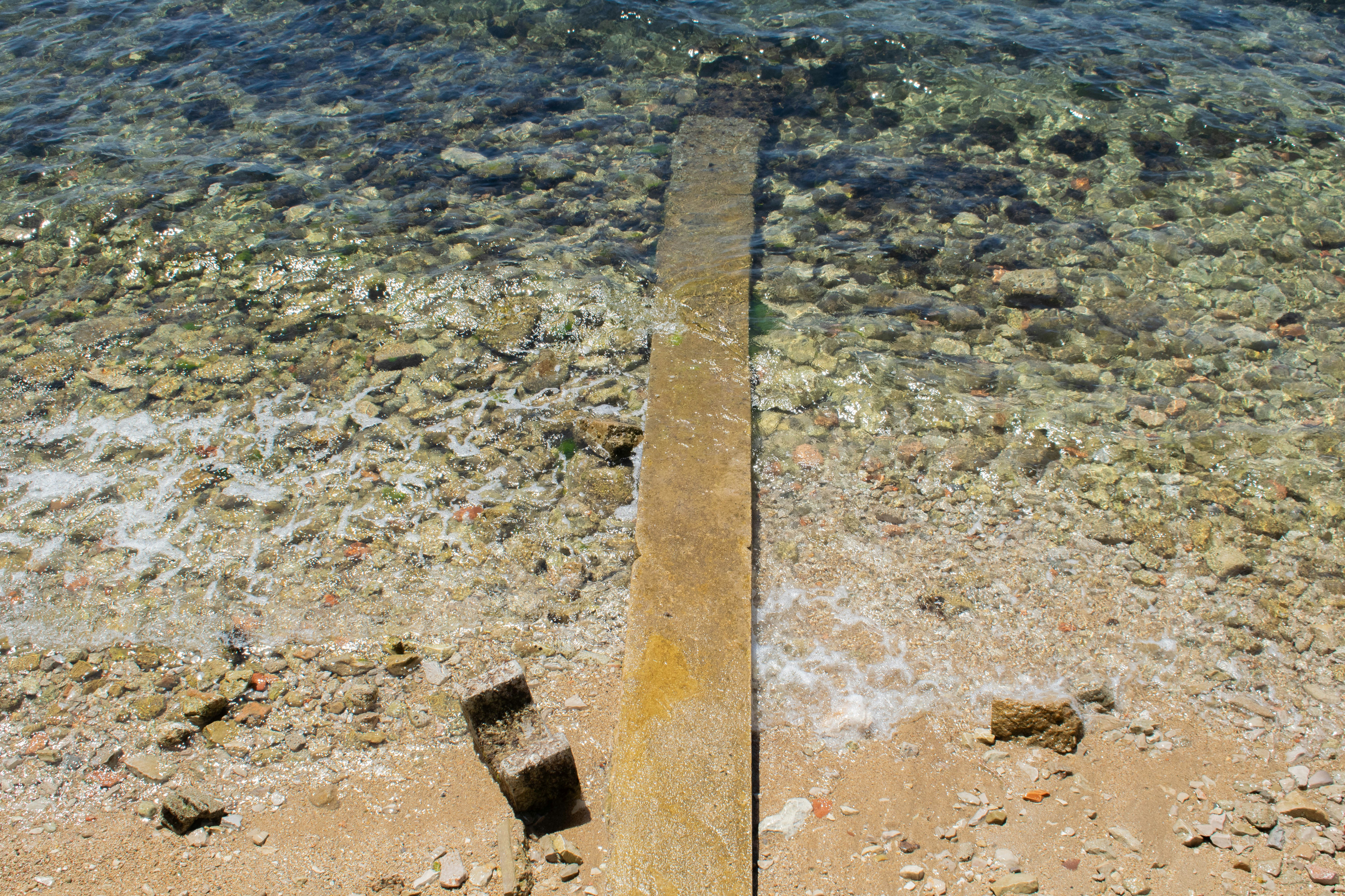 A concrete pier extending into clear shallow water over a rocky seabed