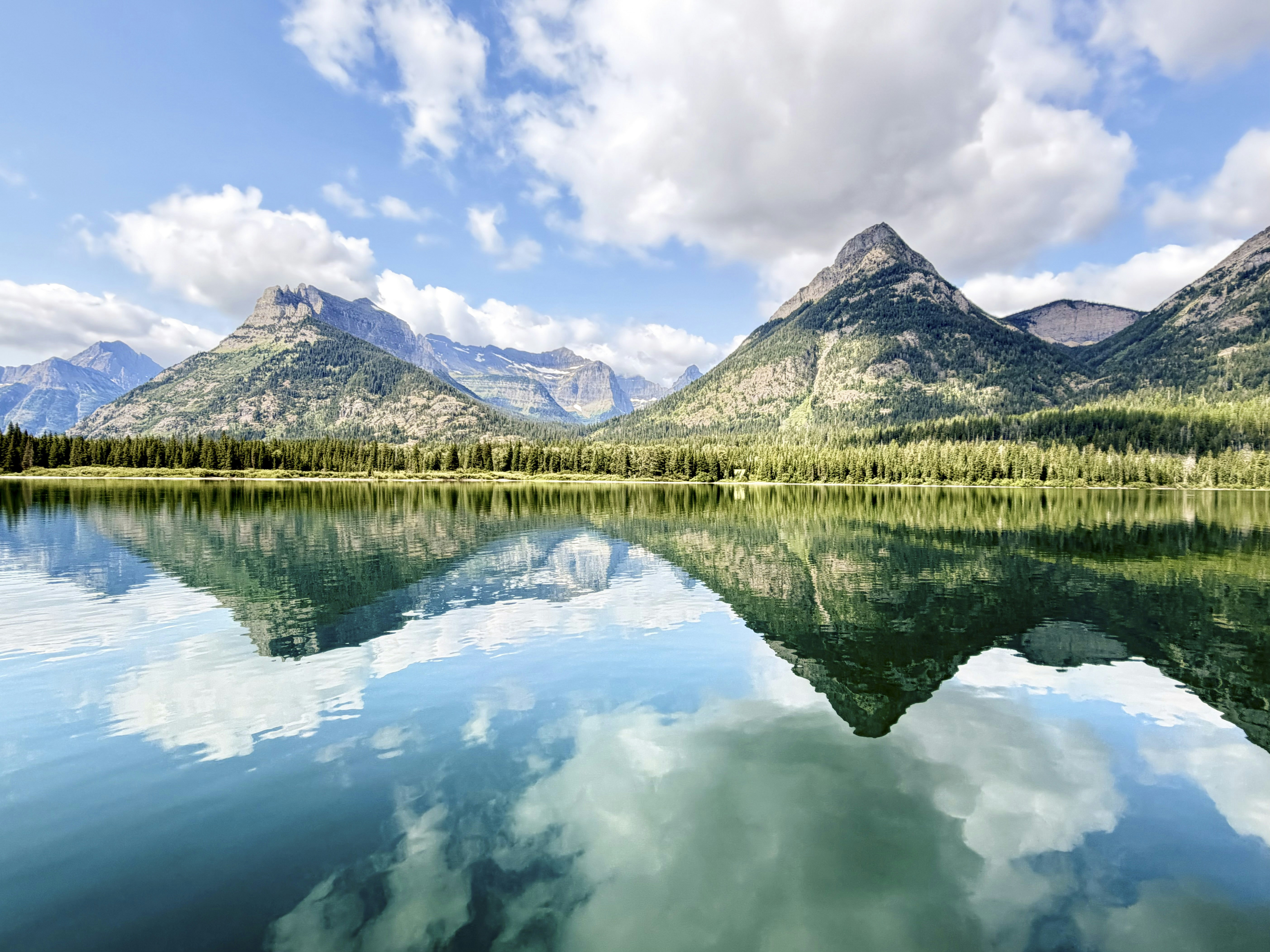 Mountains reflecting in a calm blue lake under a sky with white clouds