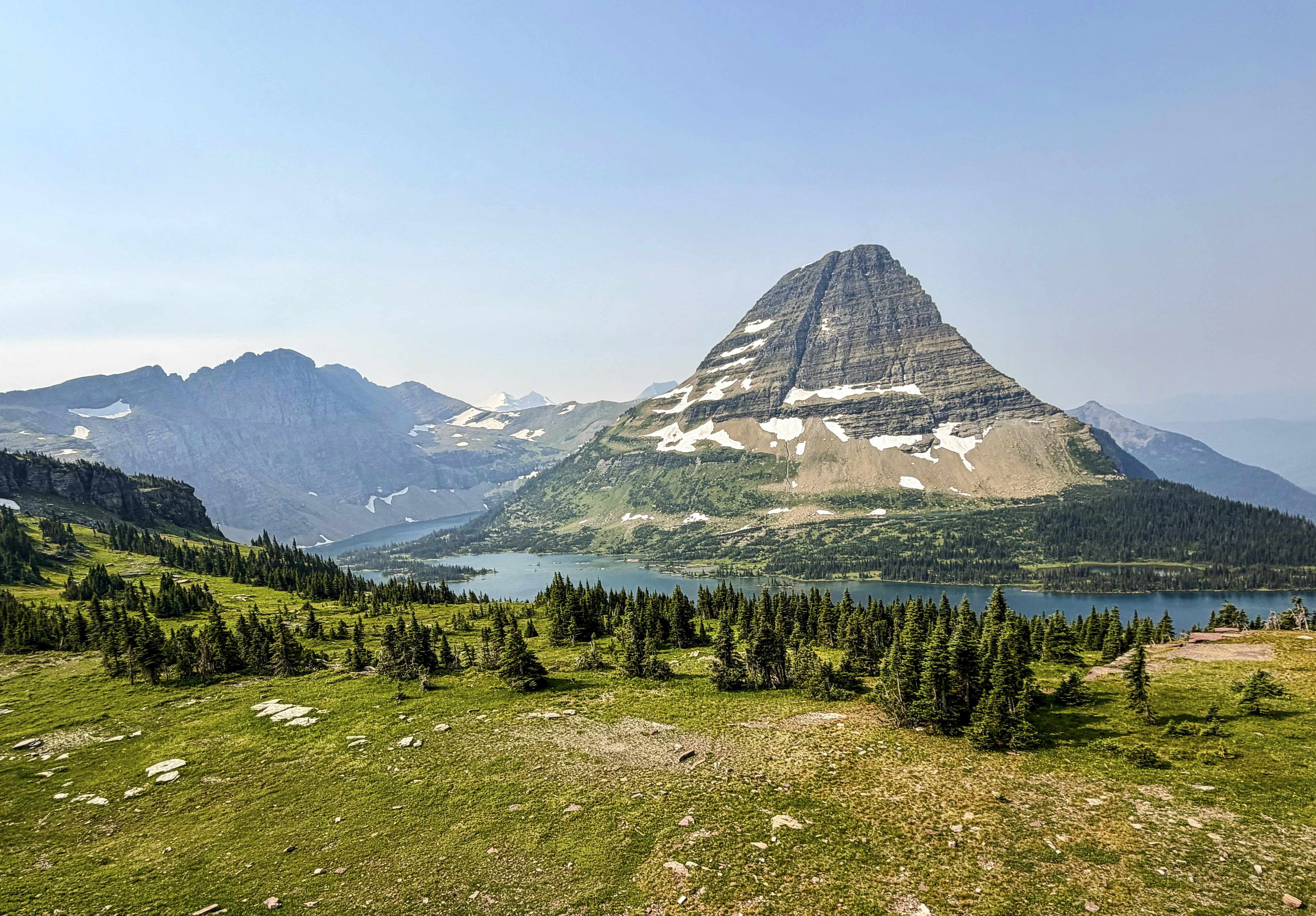 A large mountain with snow patches above a blue lake and green forest