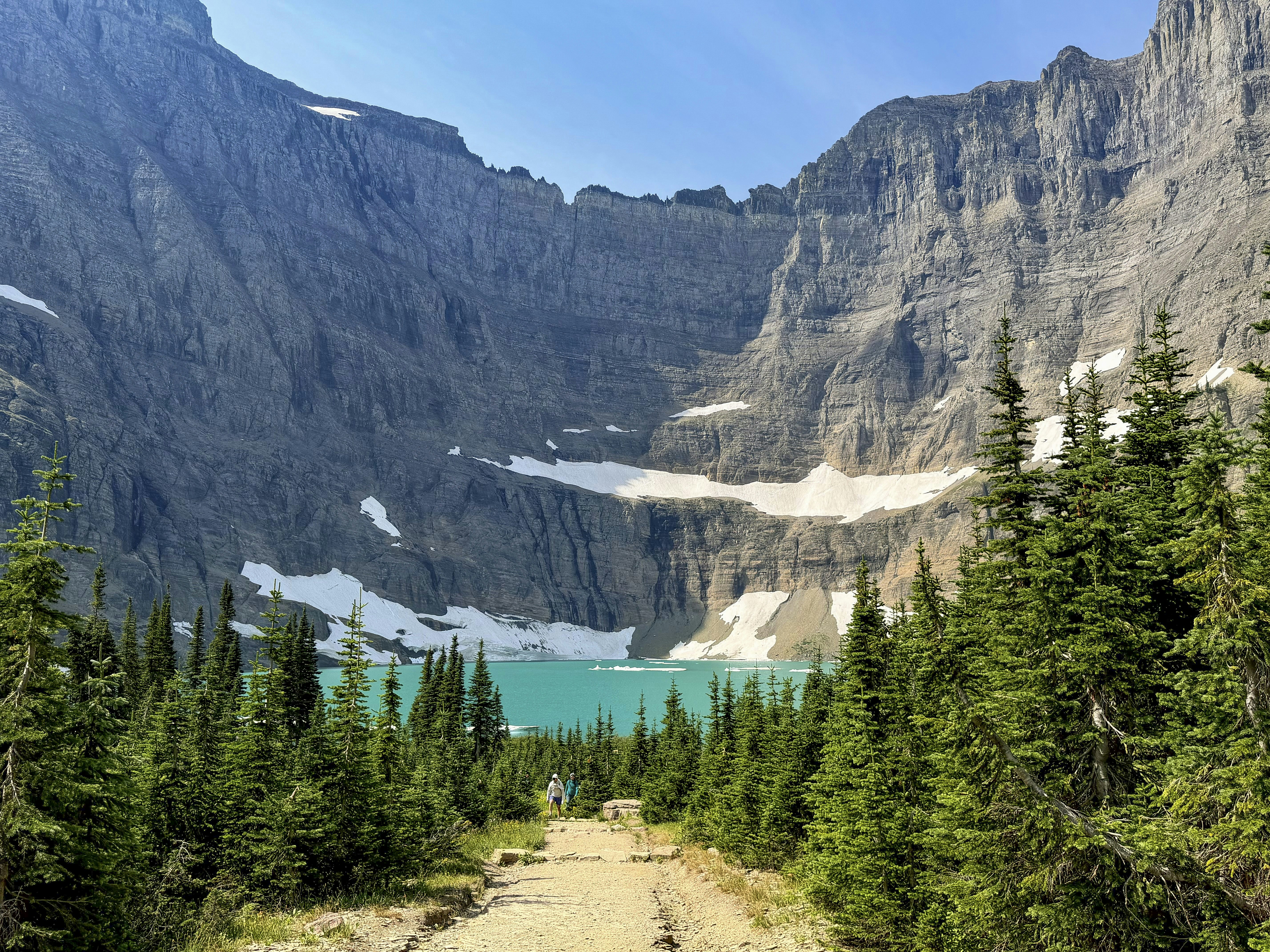A dirt trail leading toward a turquoise glacial lake surrounded by steep rocky cliffs