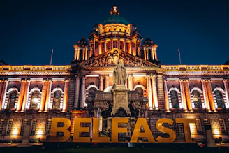 The illuminated Belfast City Hall with a large gold sign in the foreground