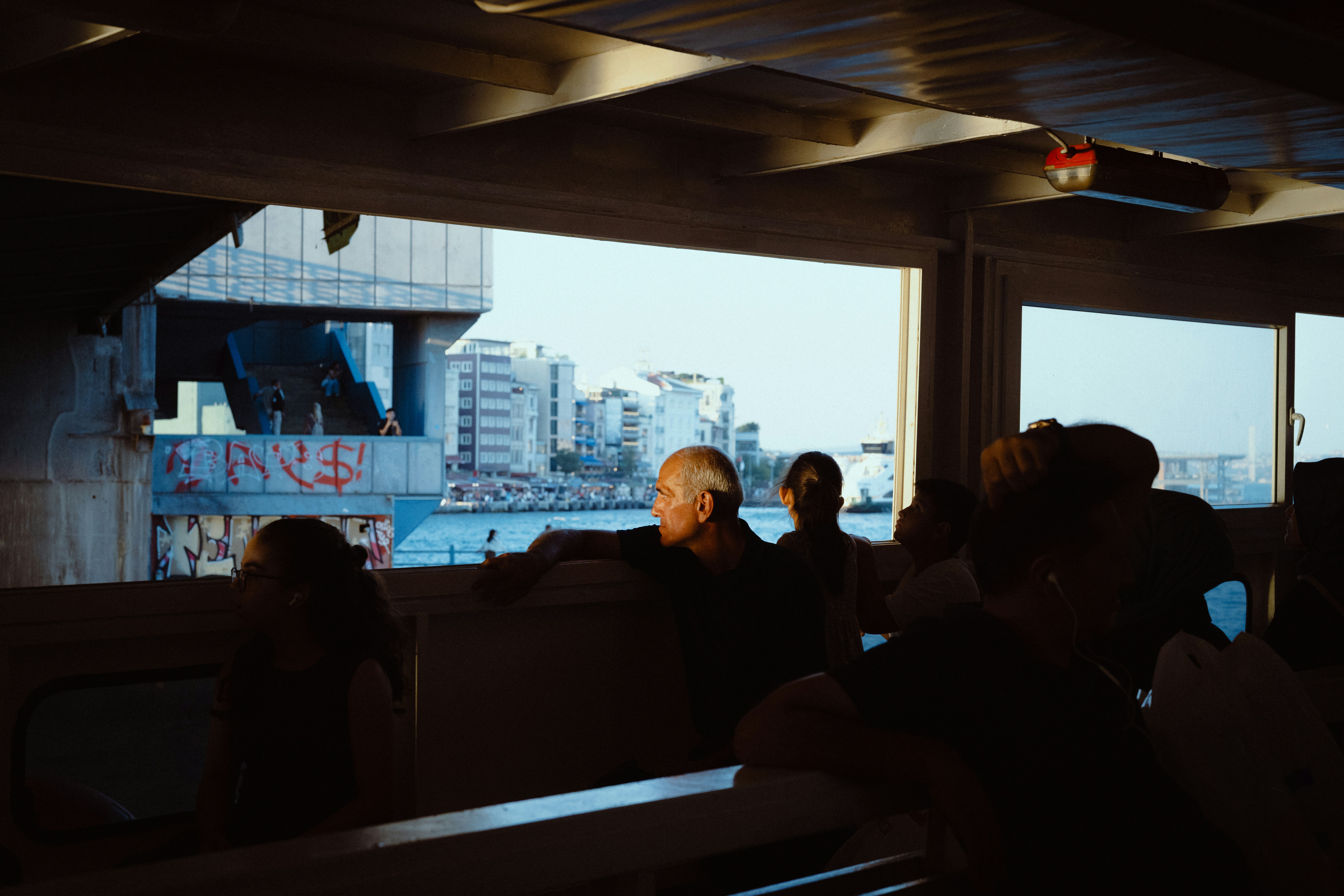 People looking out from a ferry window at a city waterfront with graffiti