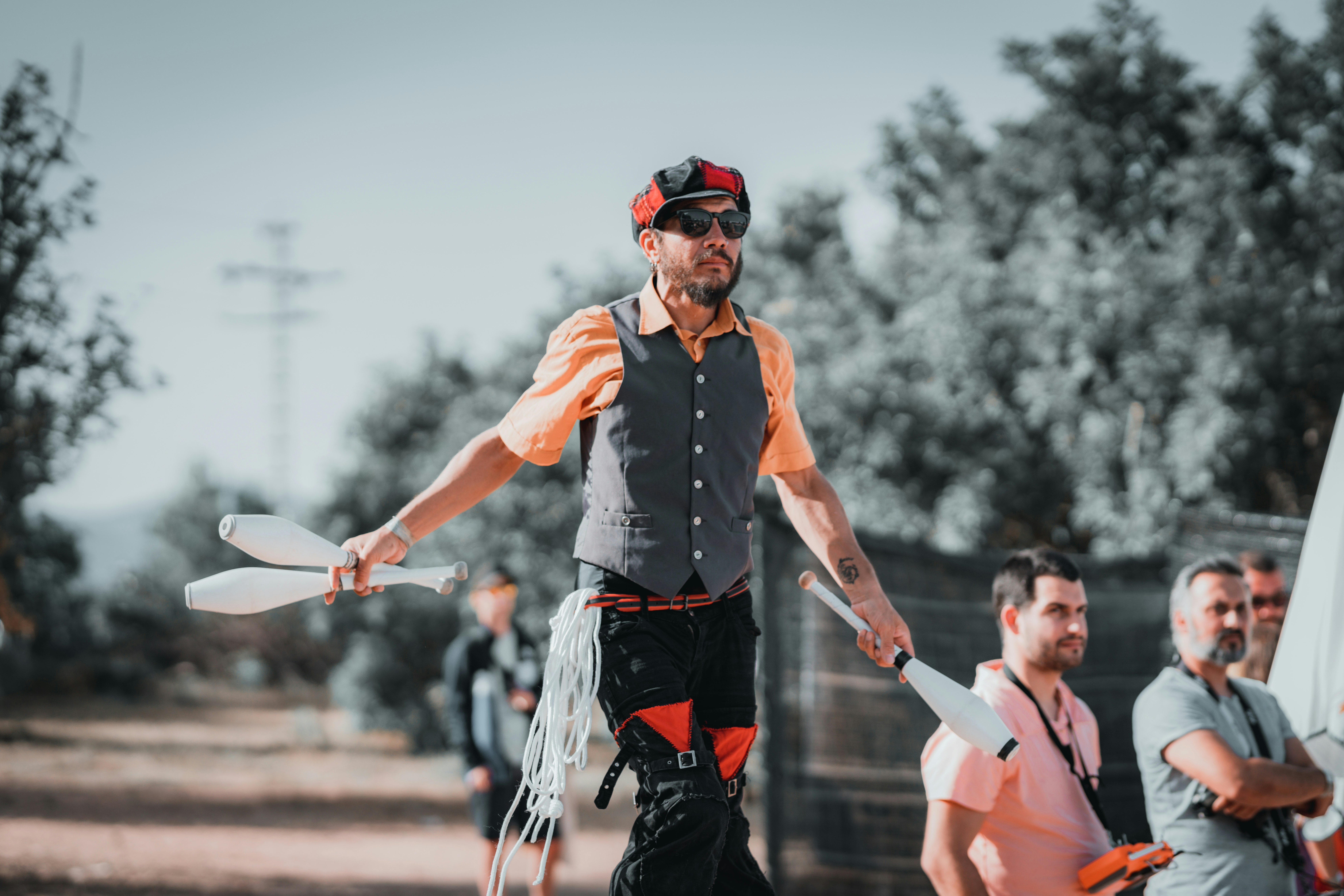 Un hombre con chaleco y gorra haciendo malabares blancos al aire libre