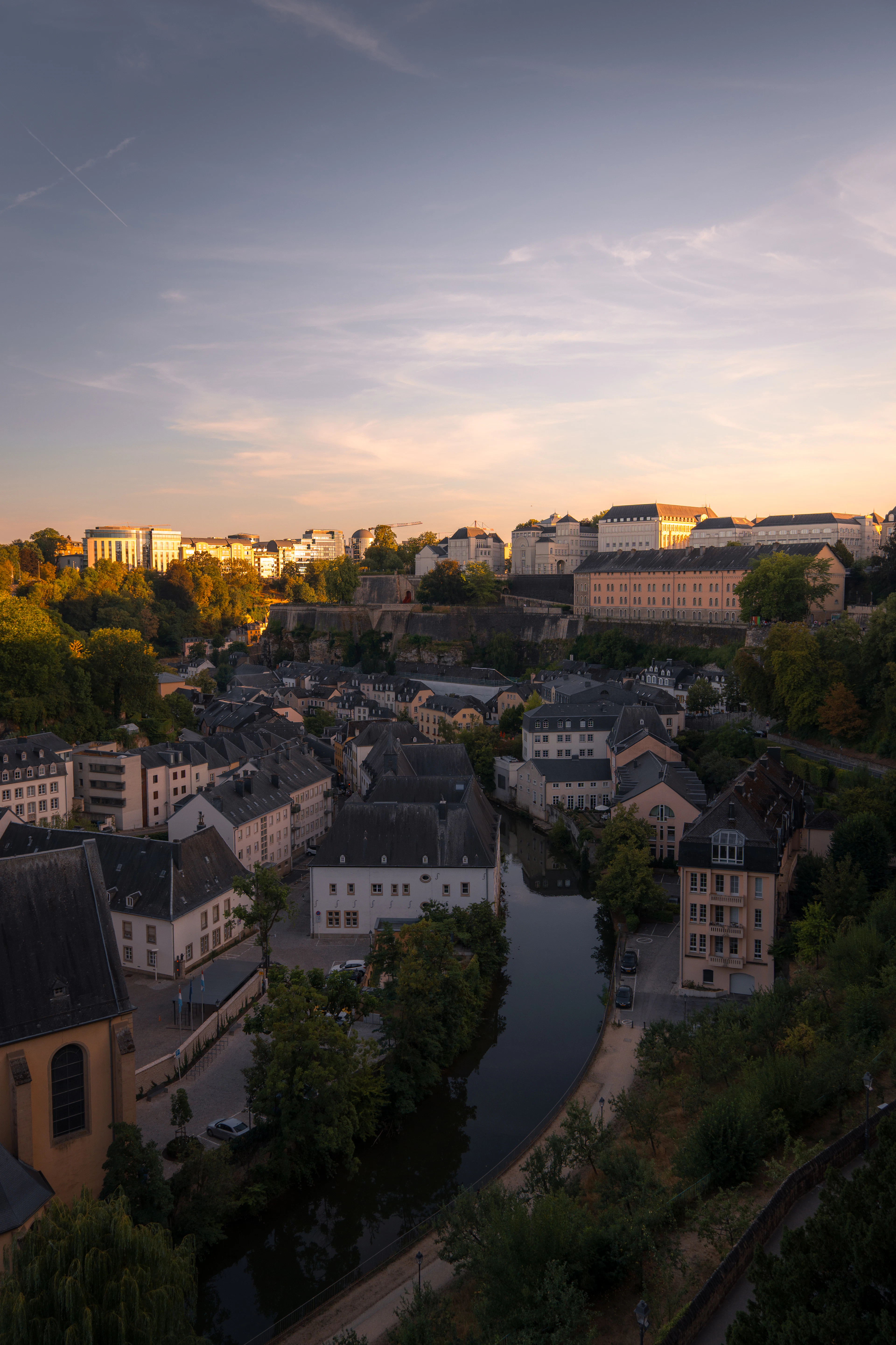 Aerial view of a river valley neighborhood with terracotta rooftops glowing in golden-hour light.