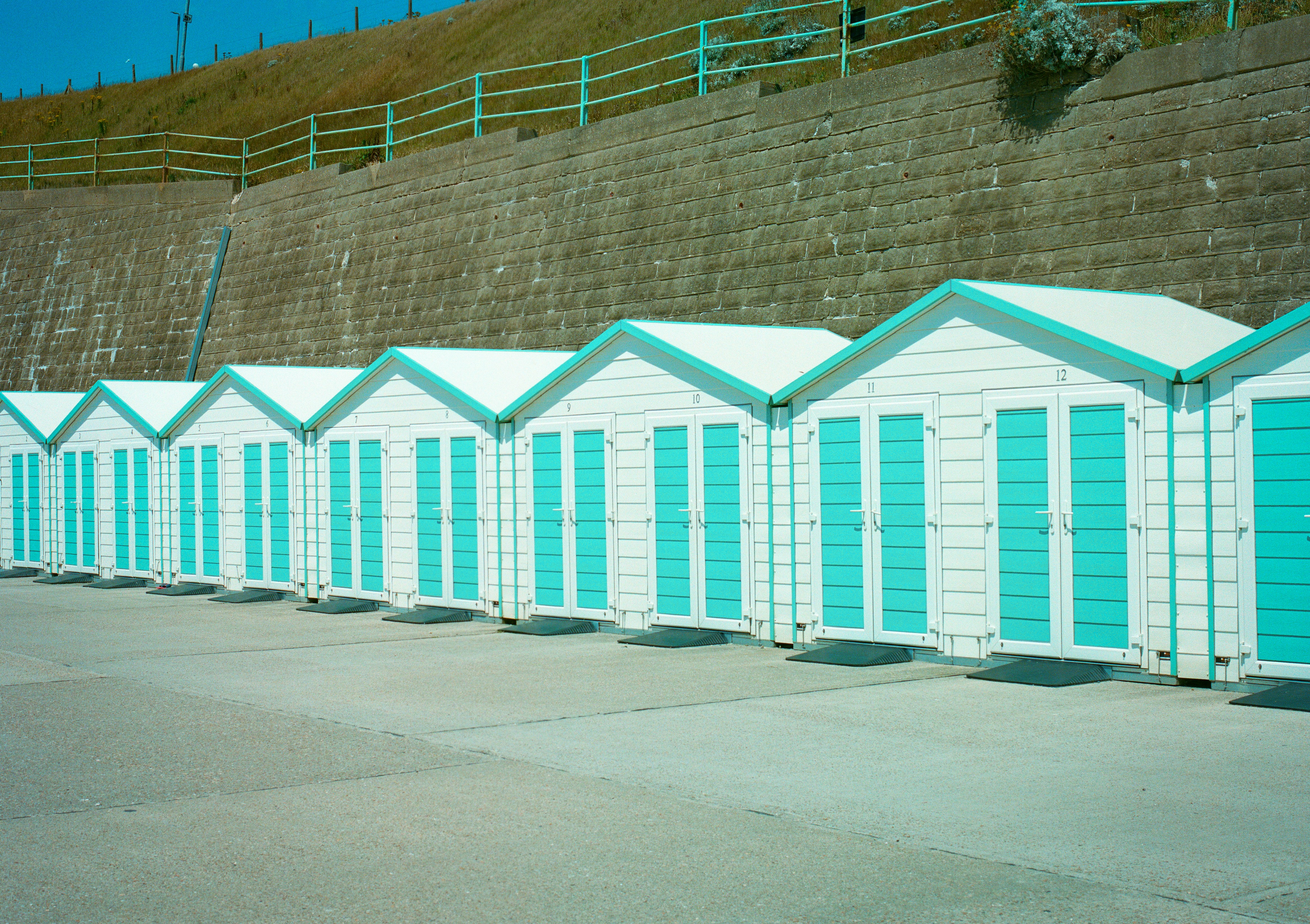 A row of white beach huts with turquoise doors against a concrete wall