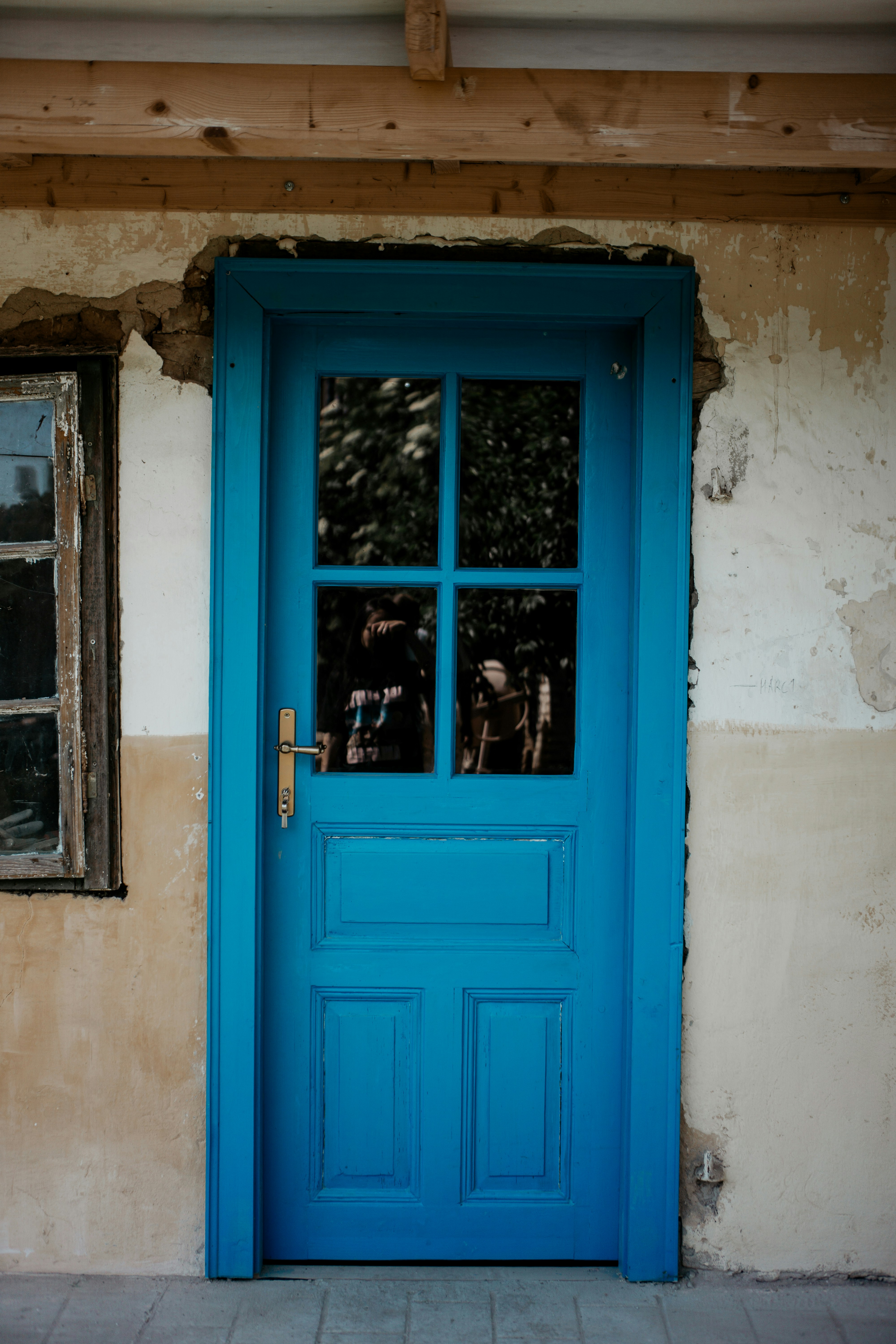 A bright blue door with glass panes in a weathered plaster wall