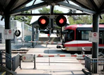 A red and white train at a railway crossing with flashing red warning lights