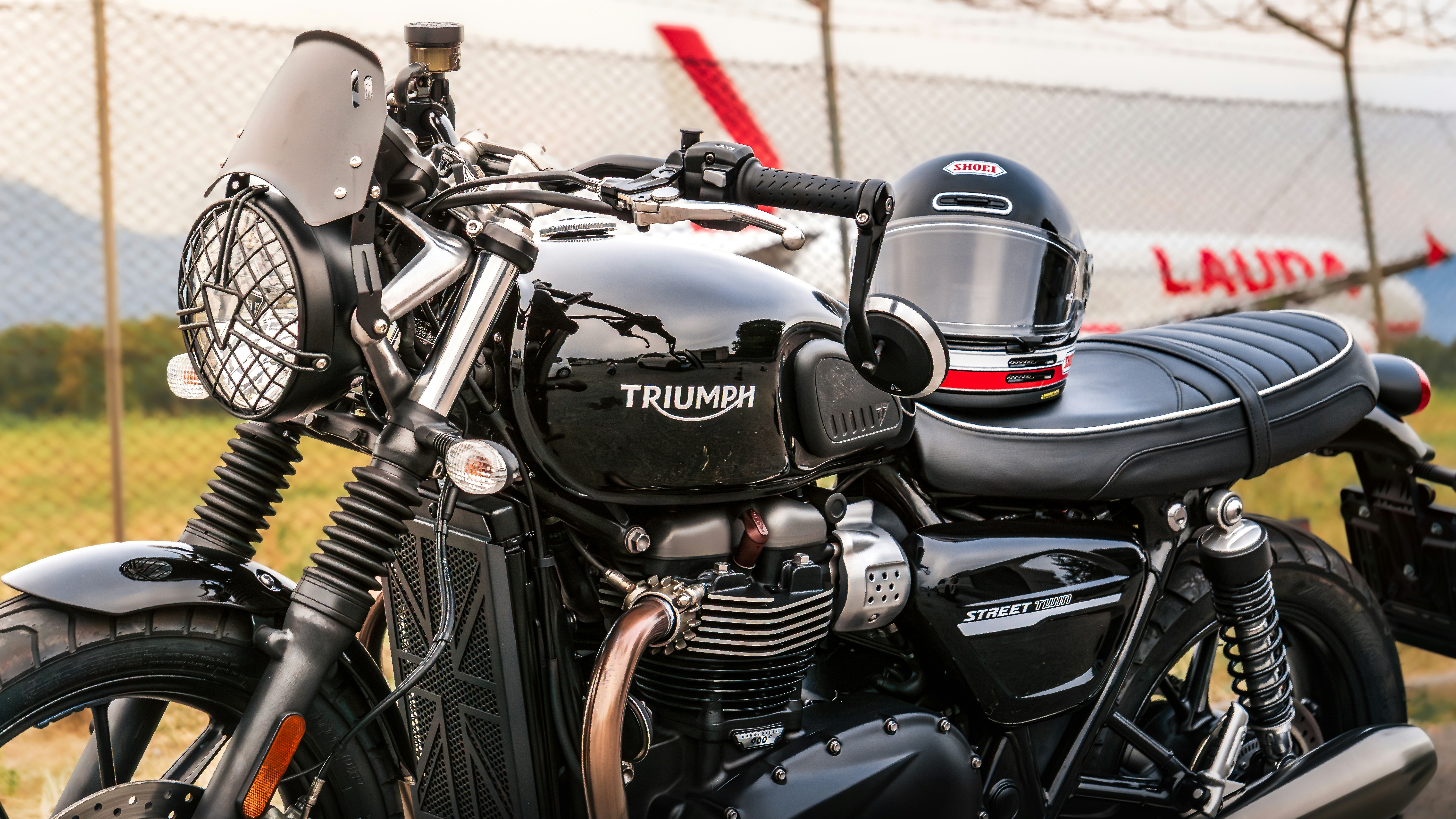 A black Triumph Street Twin motorcycle with a helmet on the seat near a fence