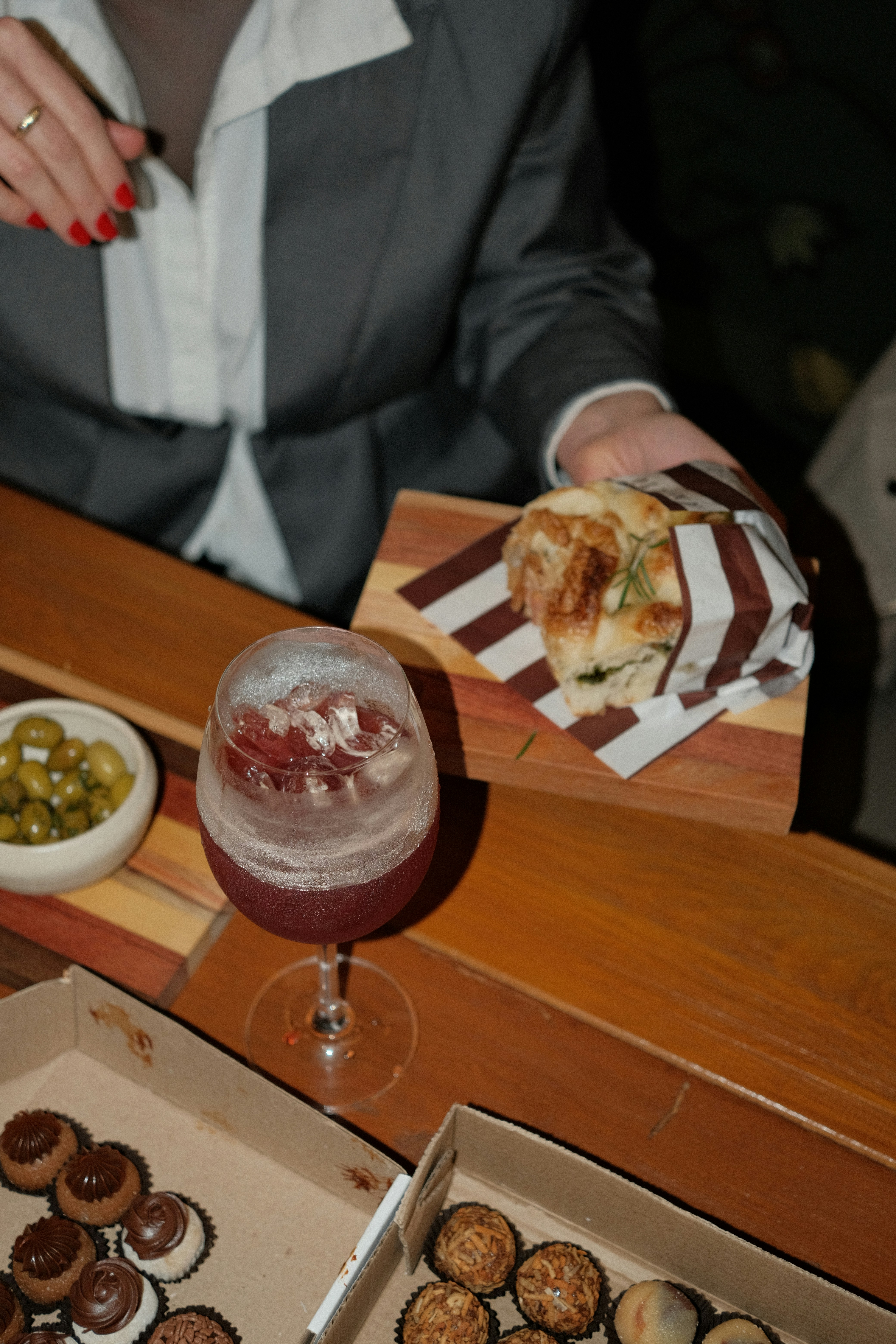 A person in a grey blazer holding a sandwich beside a red cocktail