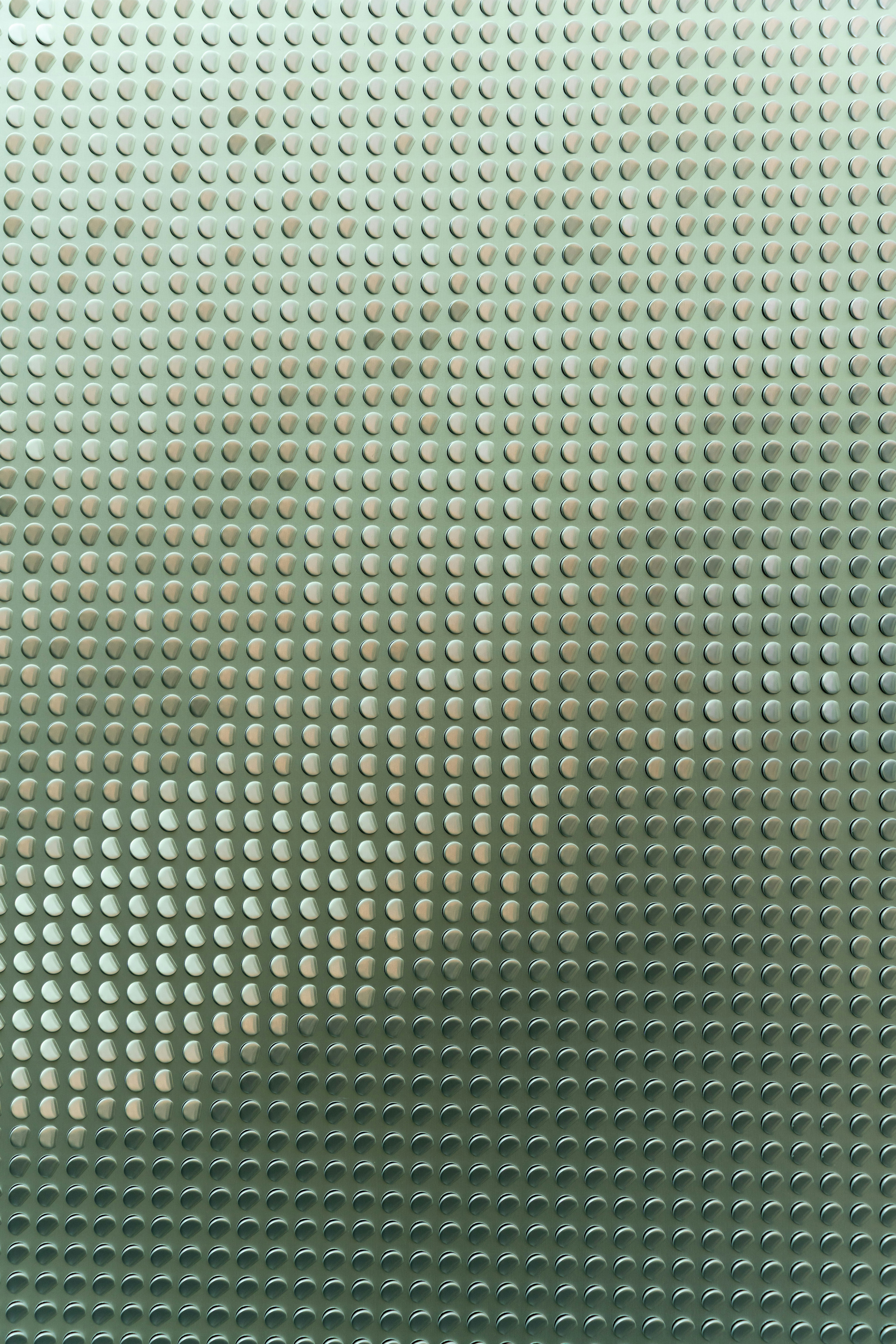 A repeating pattern of small raised metallic circles on a light green surface