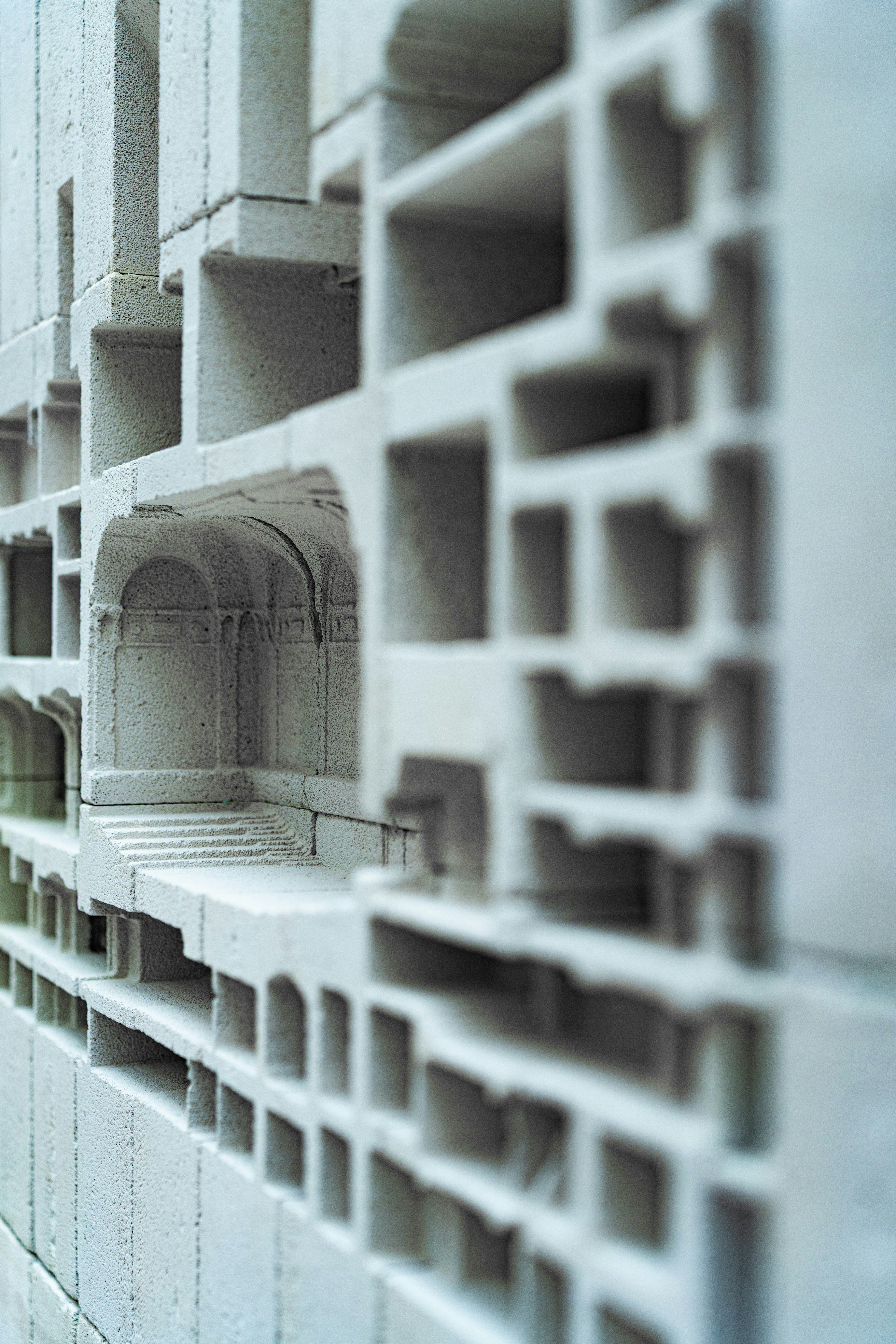 A white concrete block with a grid of recessed rectangular and arched architectural compartments