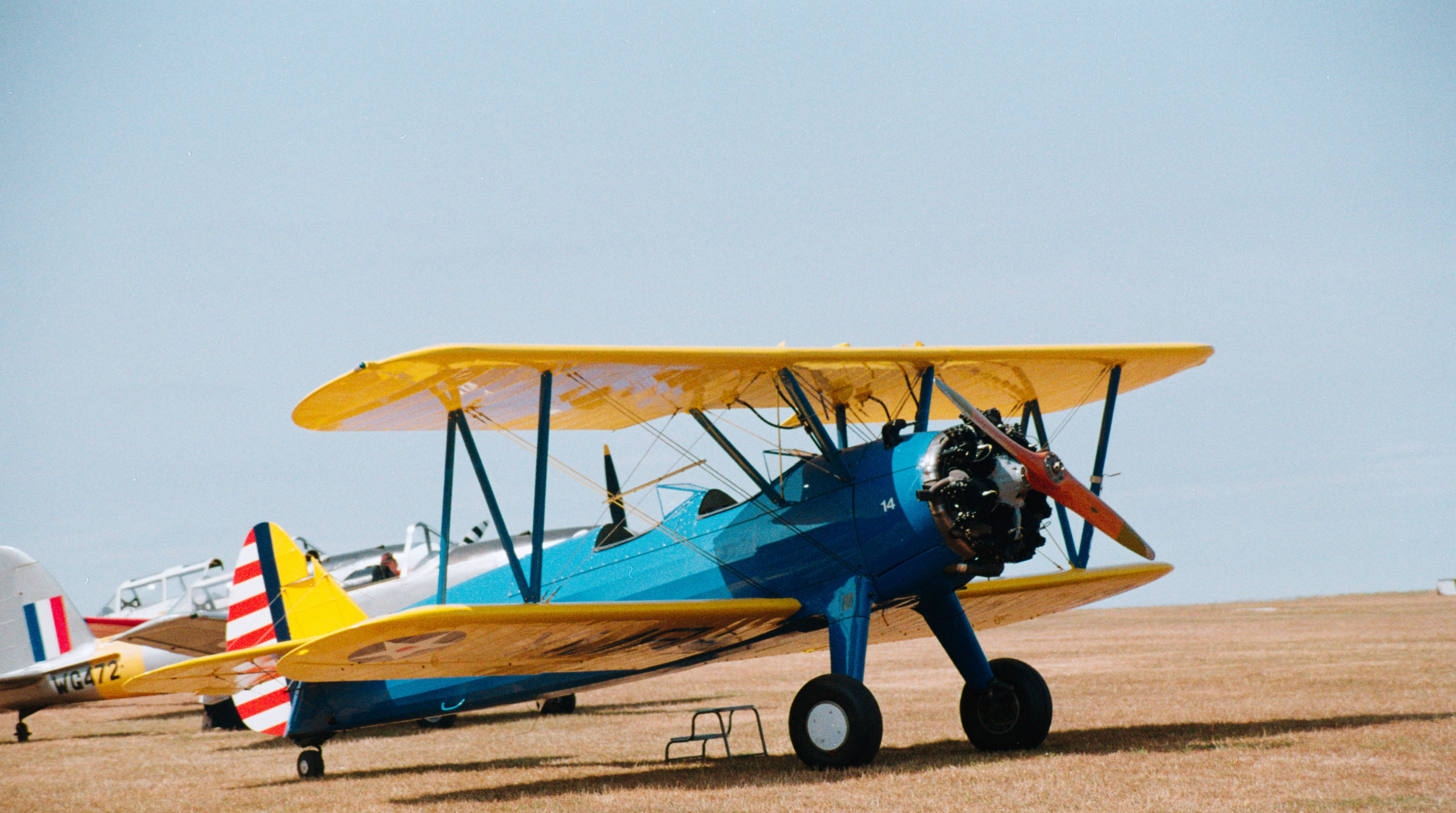 A blue and yellow biplane parked on a dry grass airfield