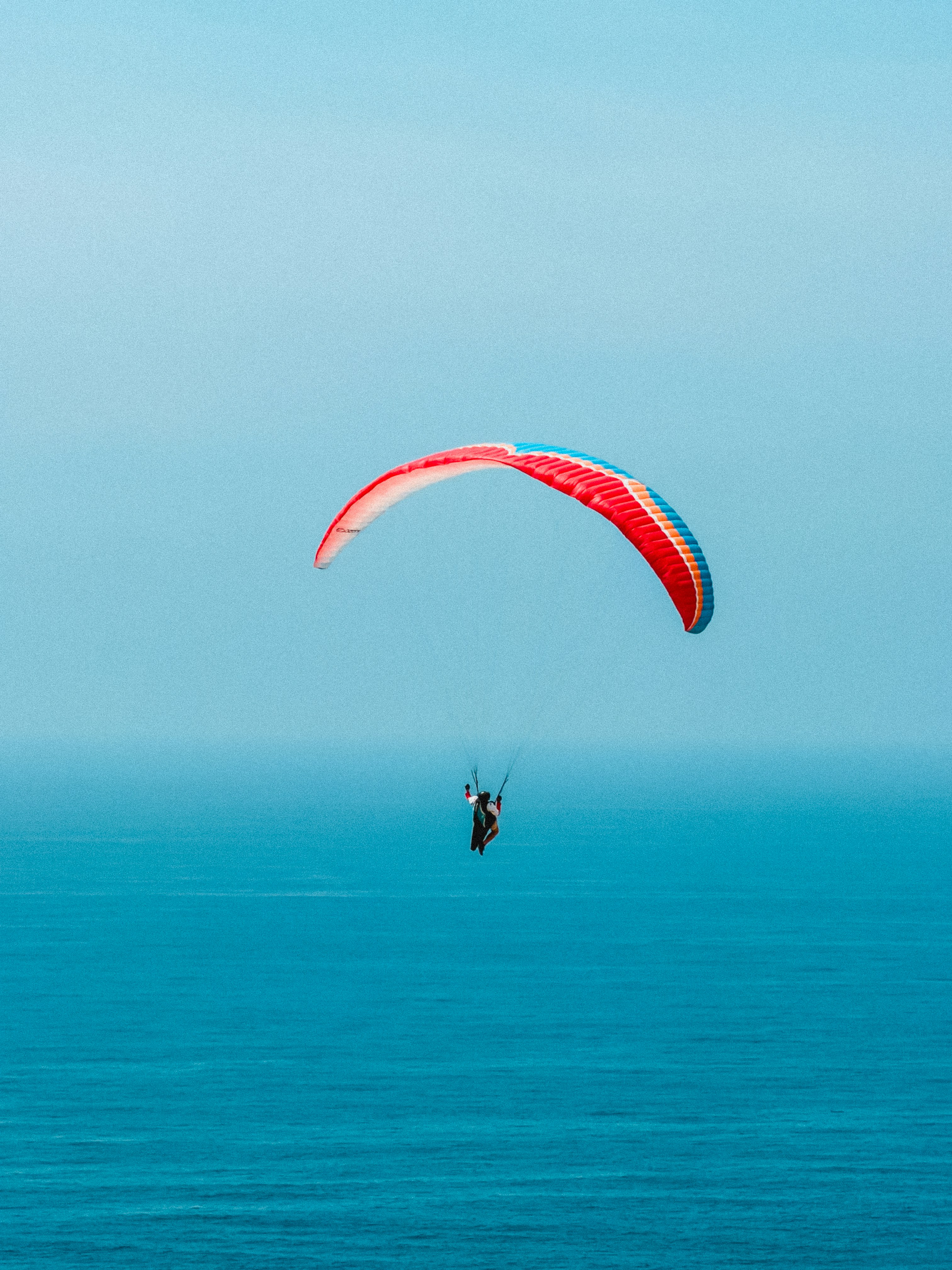 A person paragliding with a red and blue wing above the ocean