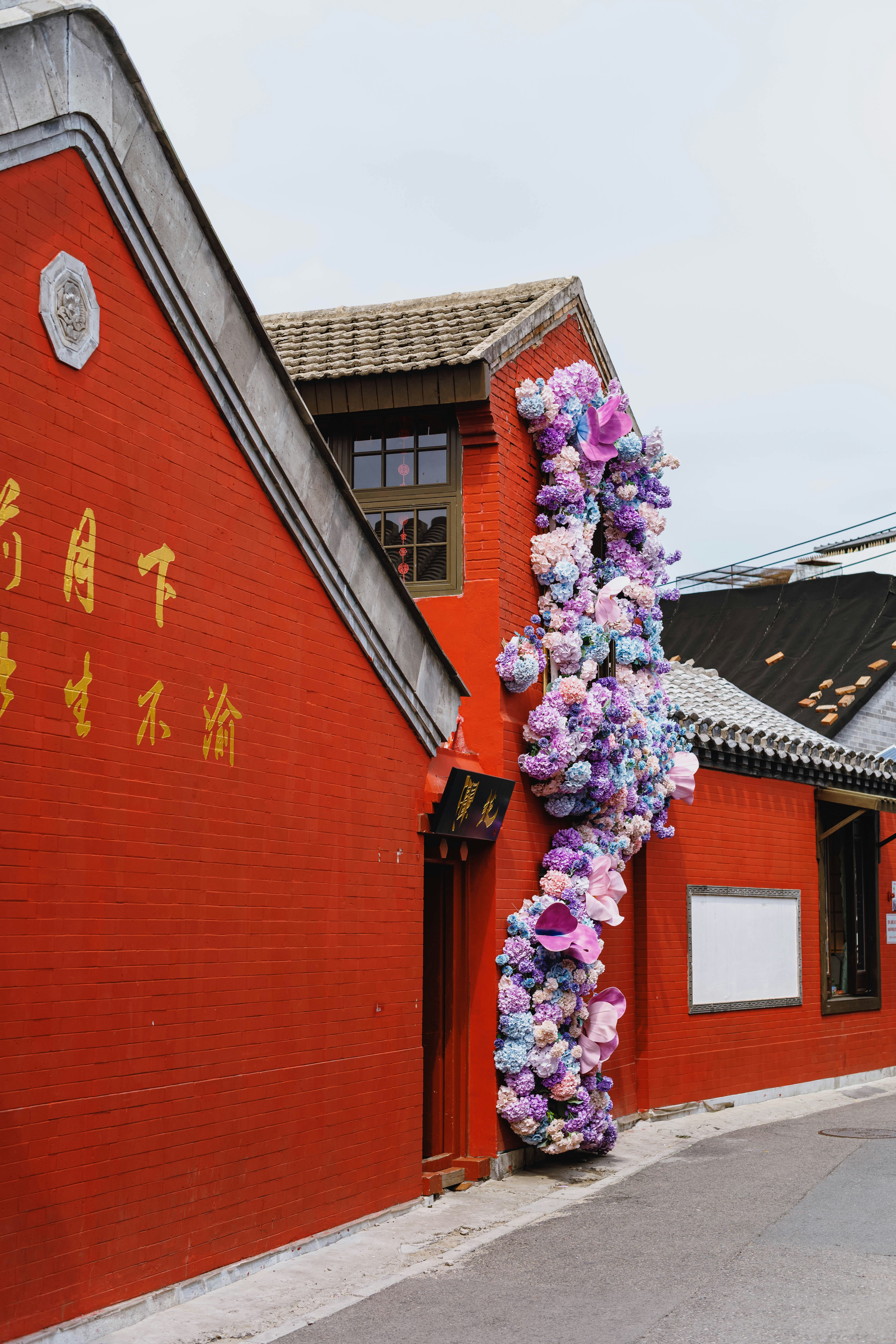 A red brick building decorated with cascading purple and pink flowers on a street