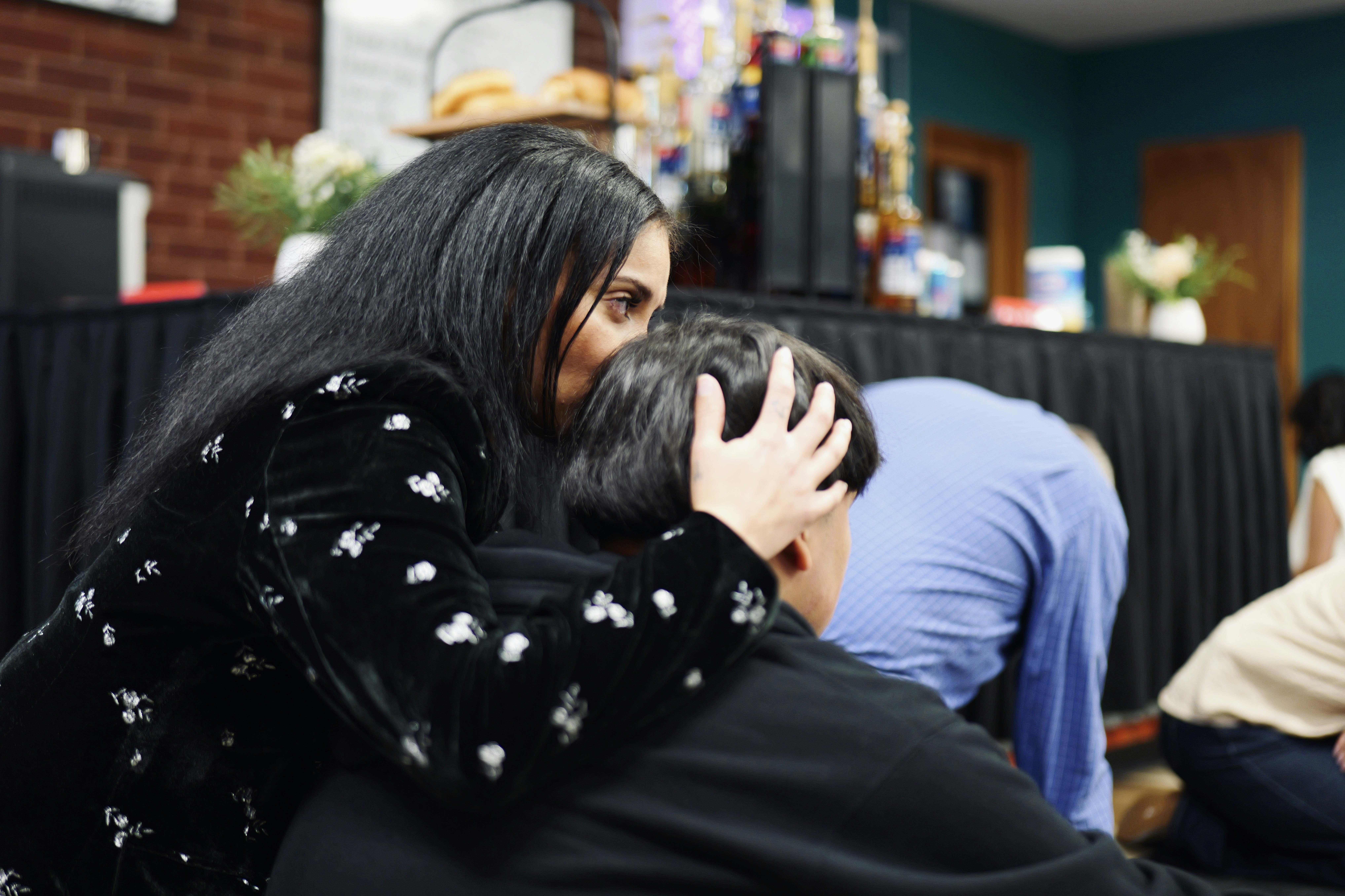 A woman with long dark hair comforting a person by holding their head