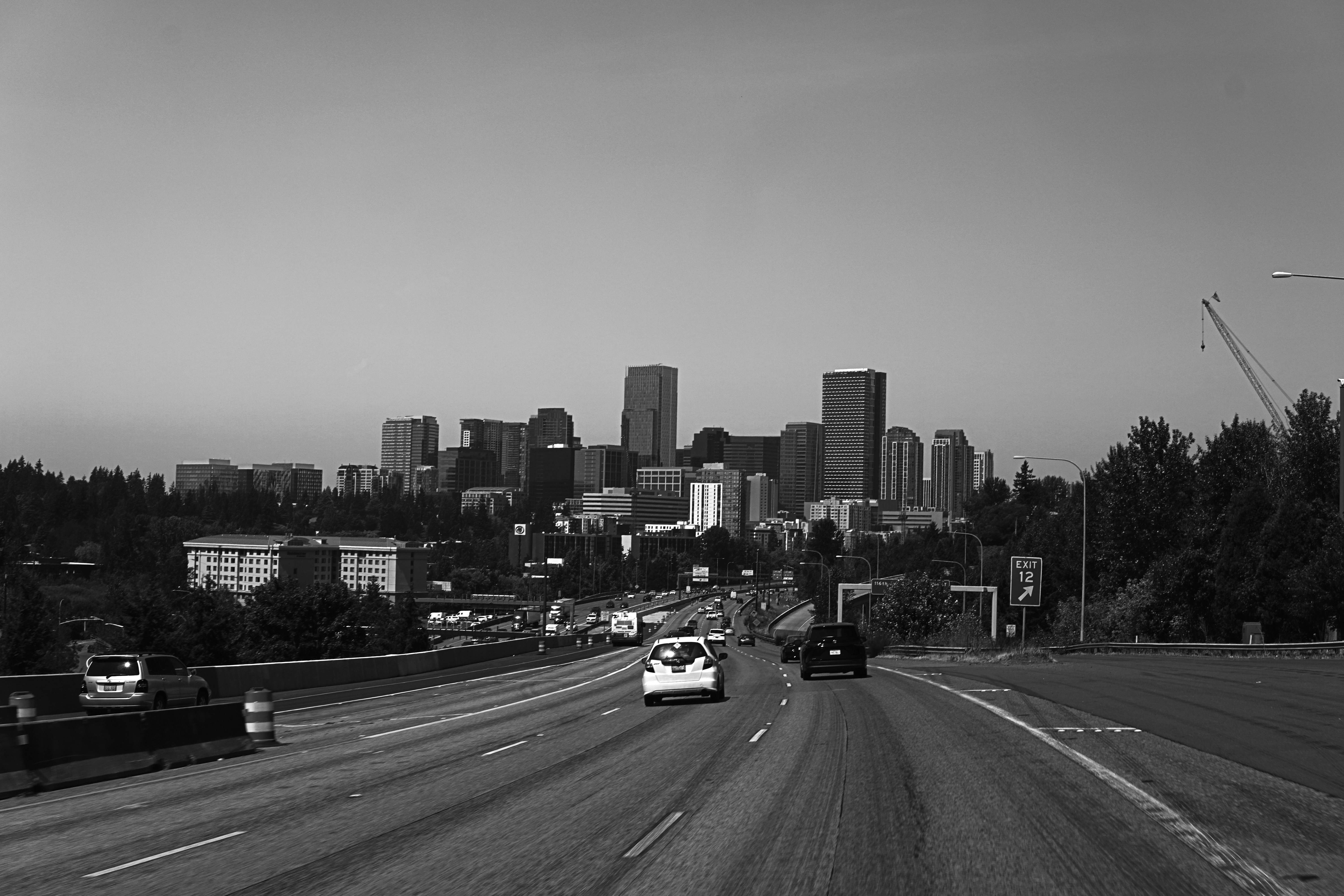 Cars driving on a highway toward a city skyline in black and white
