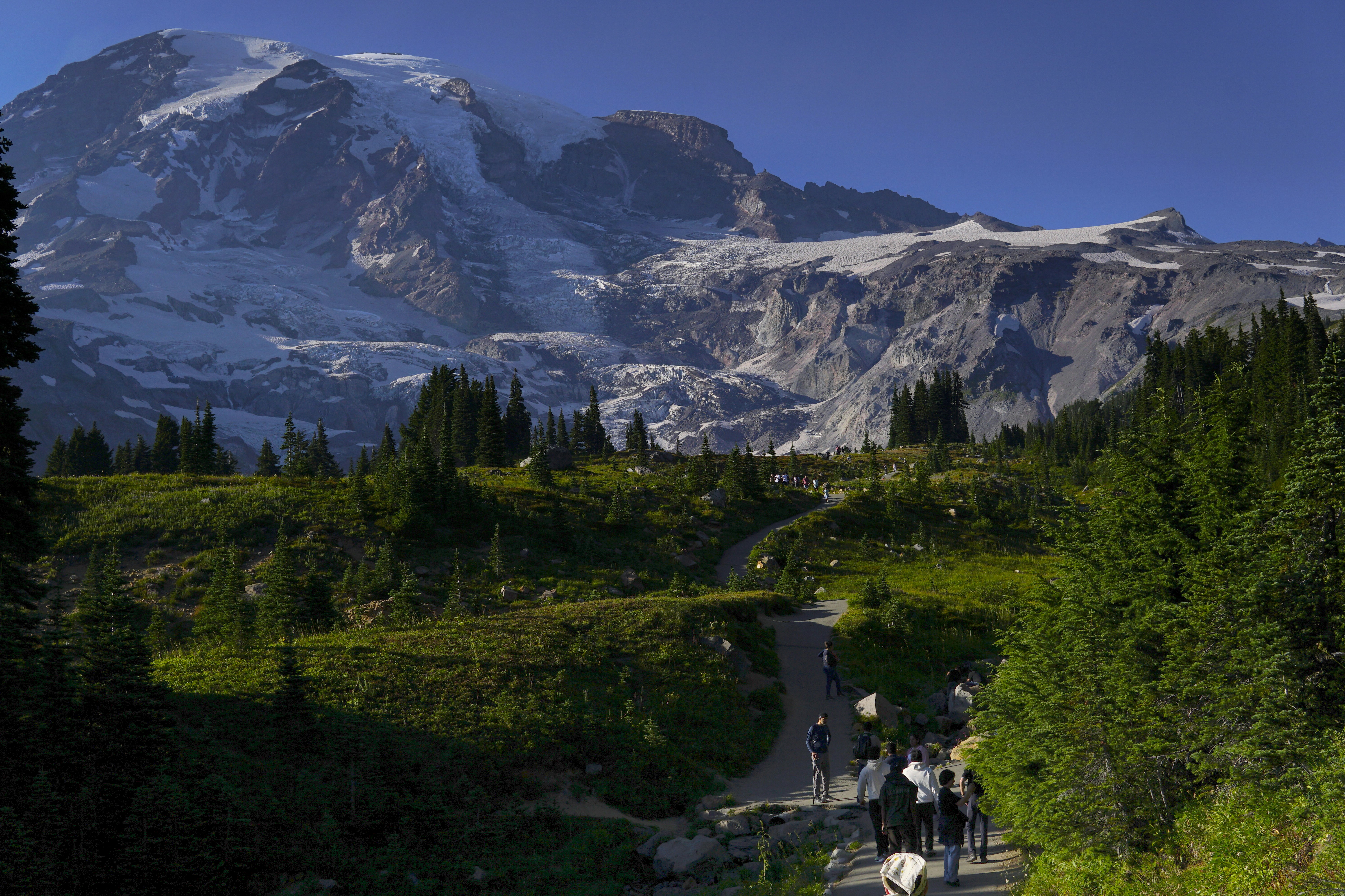 A group of people walking on a trail toward a snow-capped mountain peak