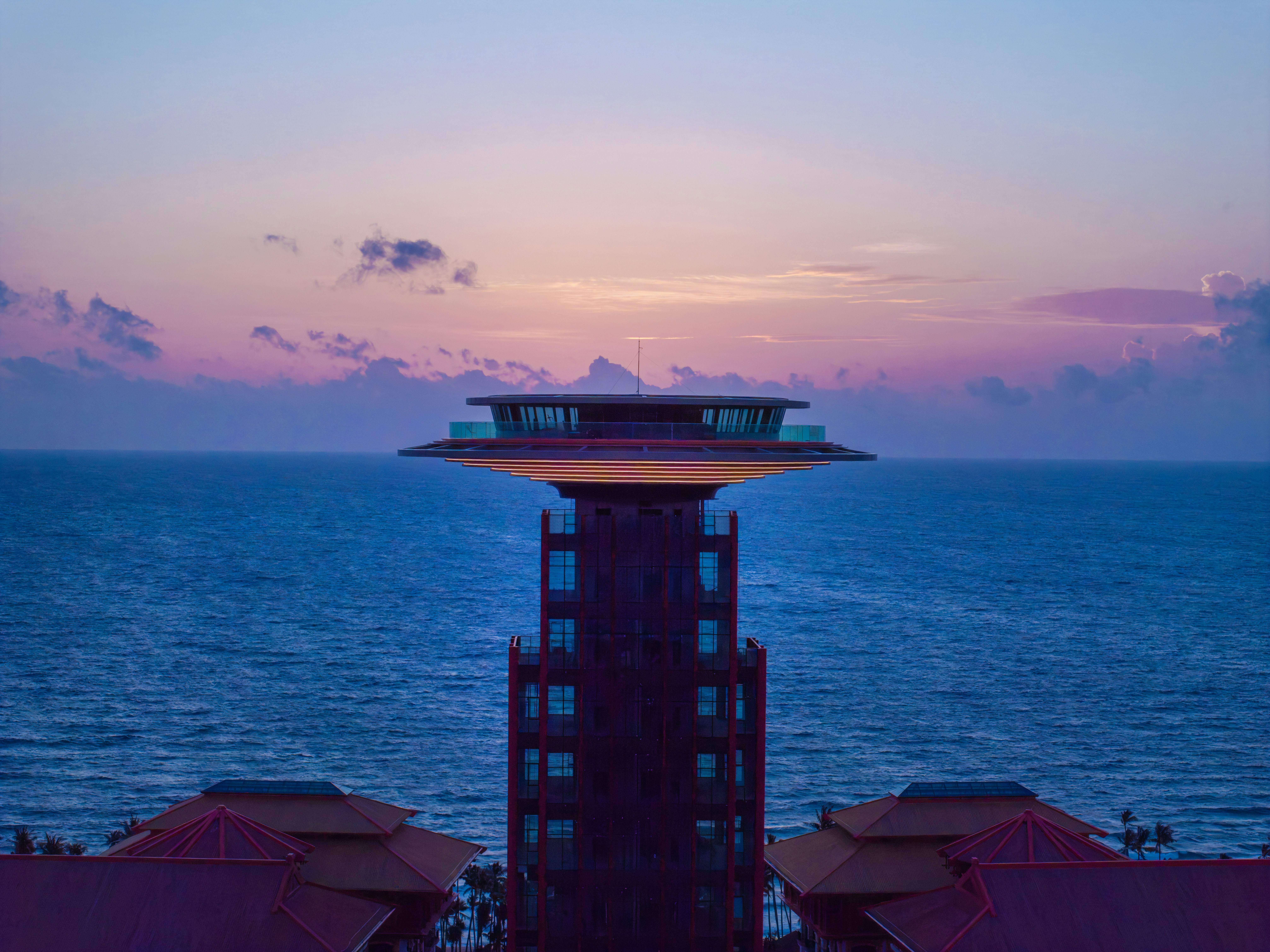 A tall red tower with a circular observation deck against a purple sky