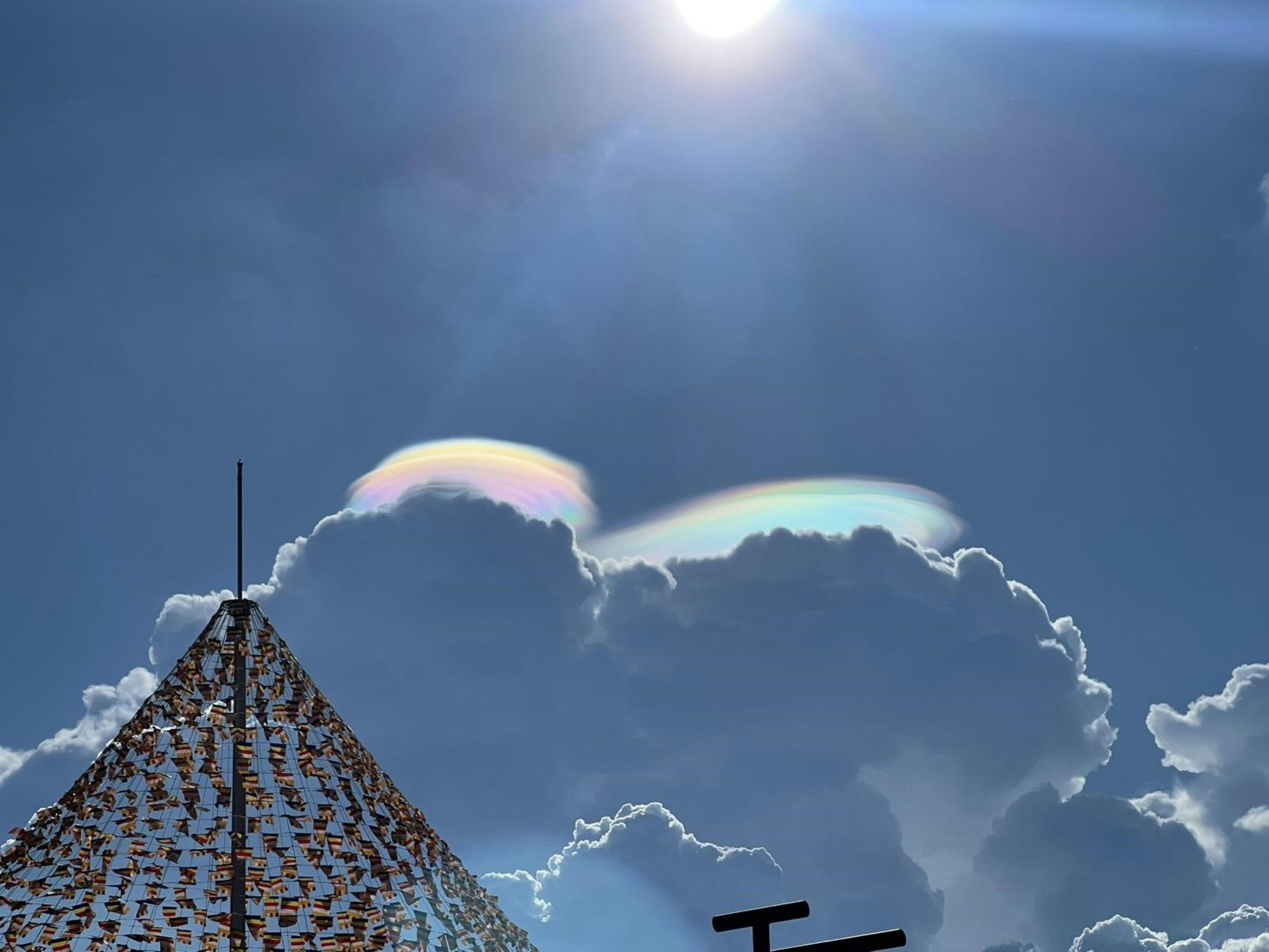 Iridescent pileus clouds above a conical structure covered in small flags