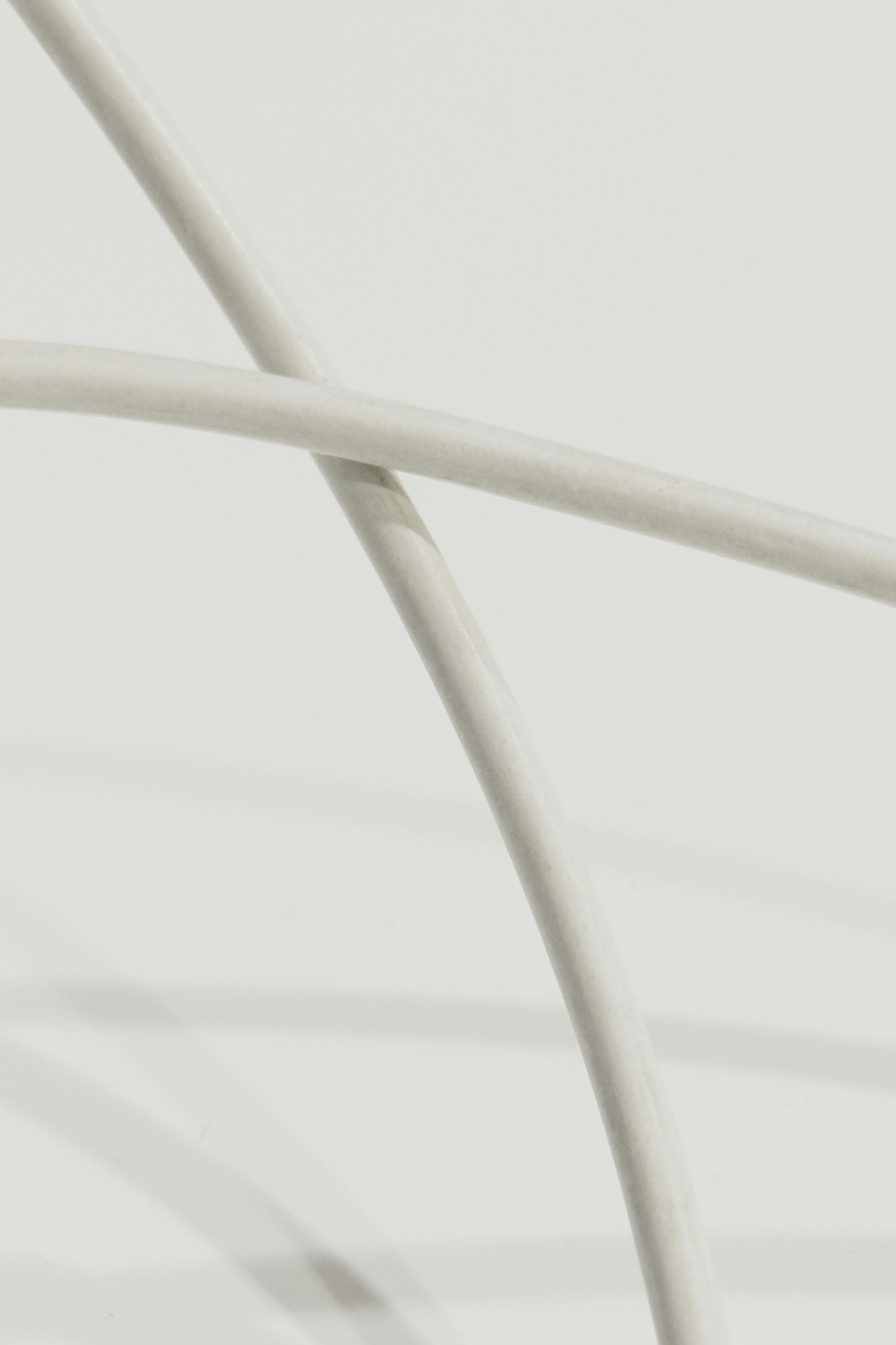 Two intersecting white curved rods casting soft shadows on a white surface