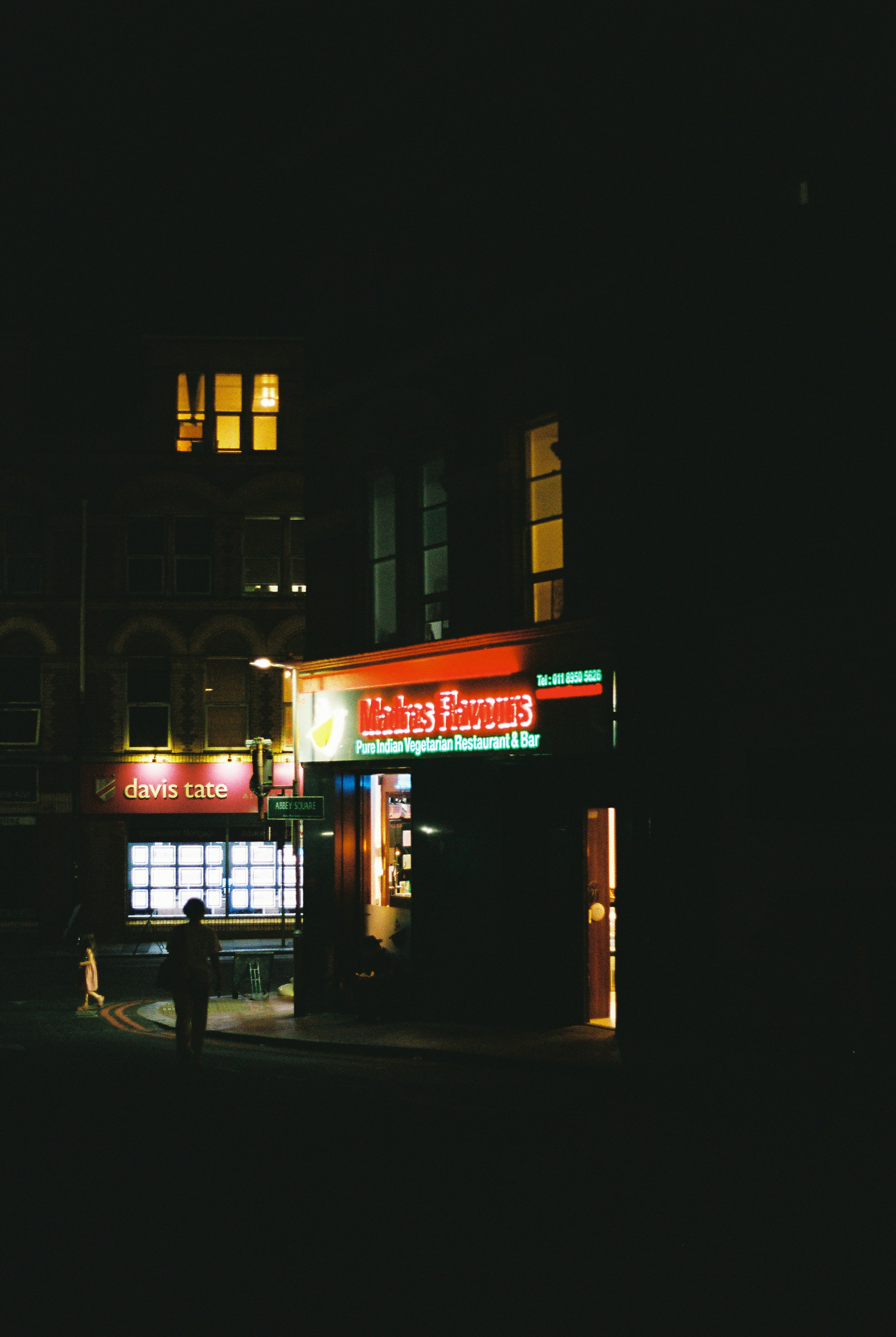 A person walking past a restaurant with a glowing sign at night