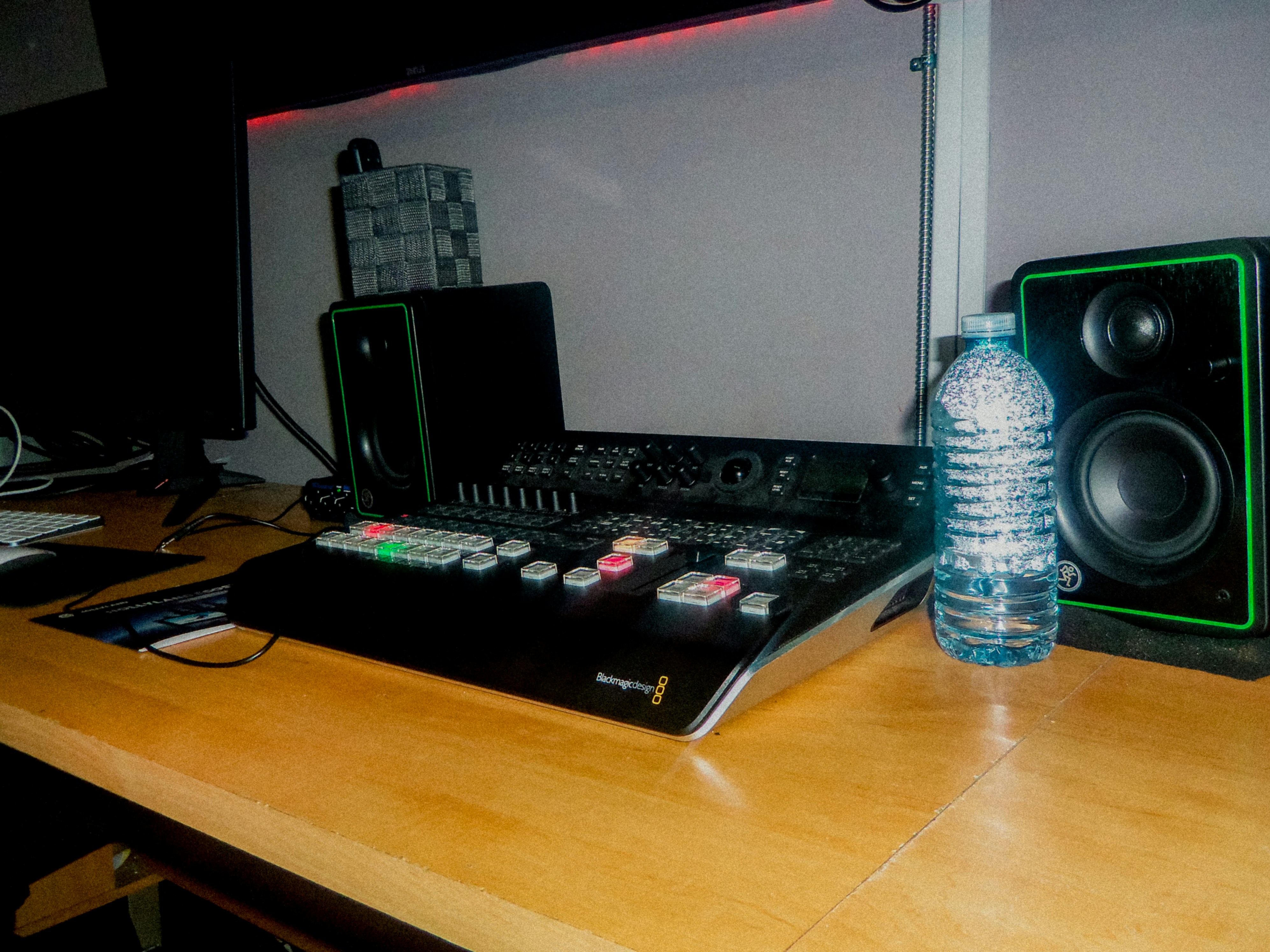 A video switcher console with illuminated buttons on a wooden desk with speakers