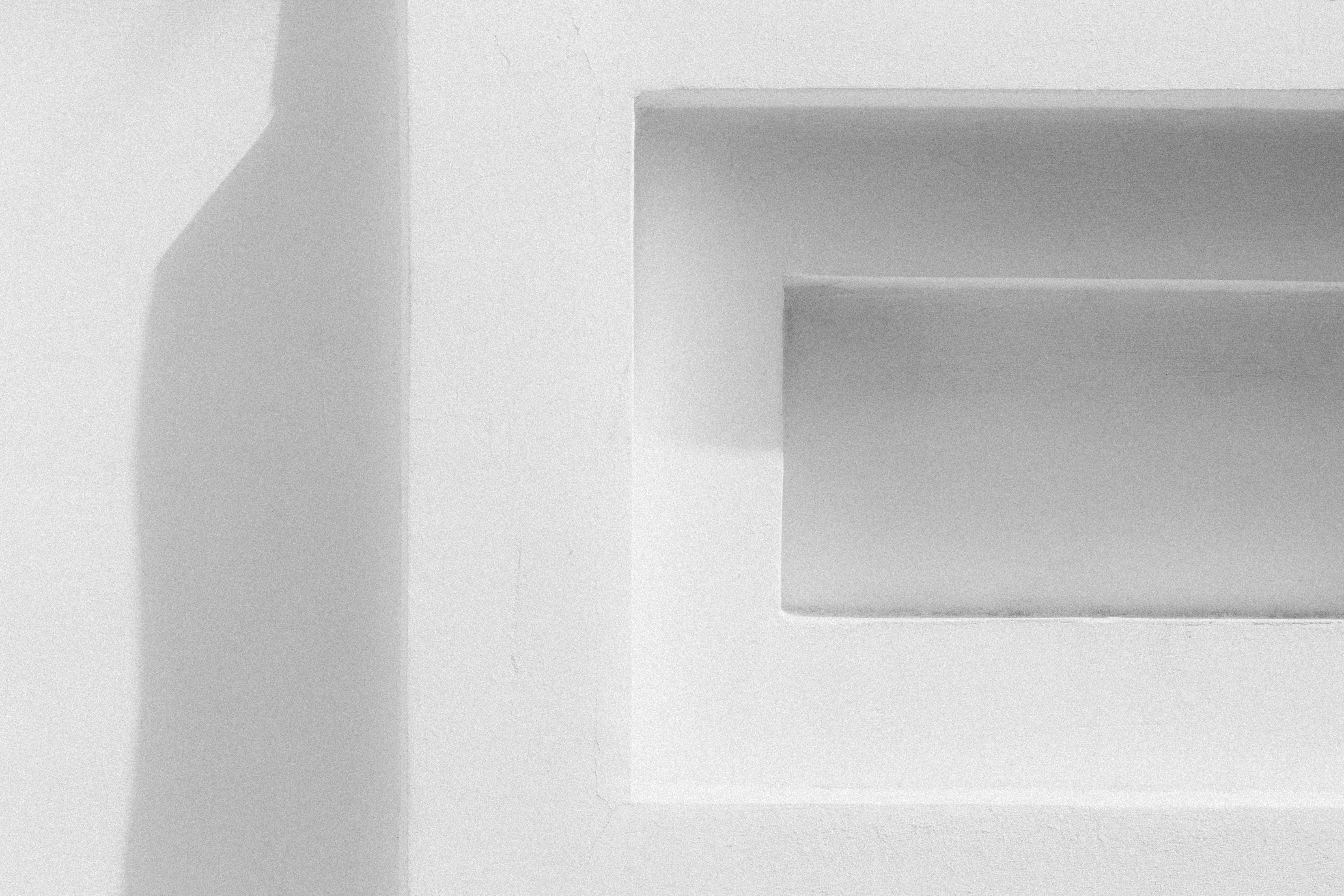 A white wall with a recessed rectangular niche and a long vertical shadow