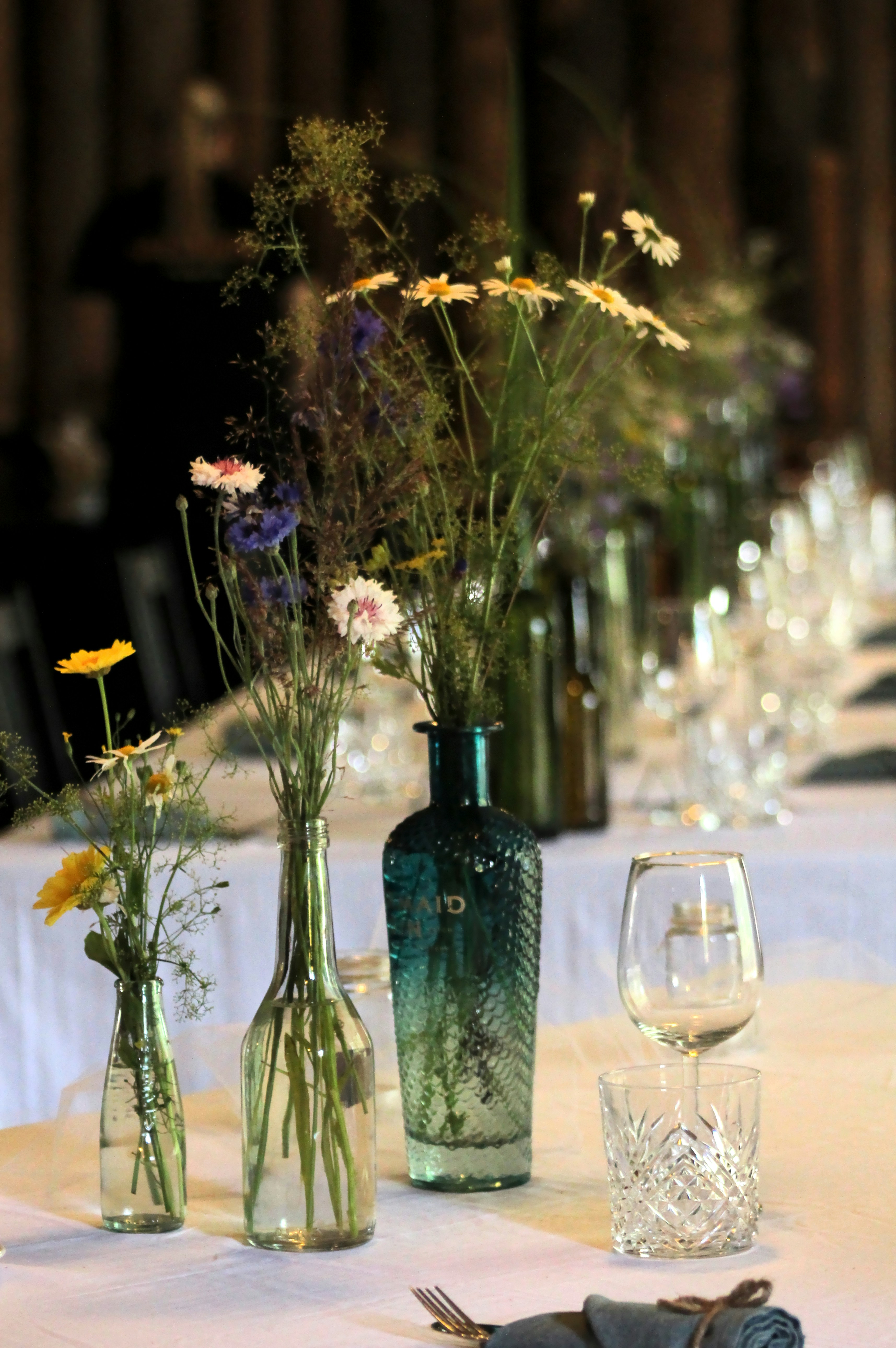 Wildflowers in glass bottles on a white tablecloth at a long dining table