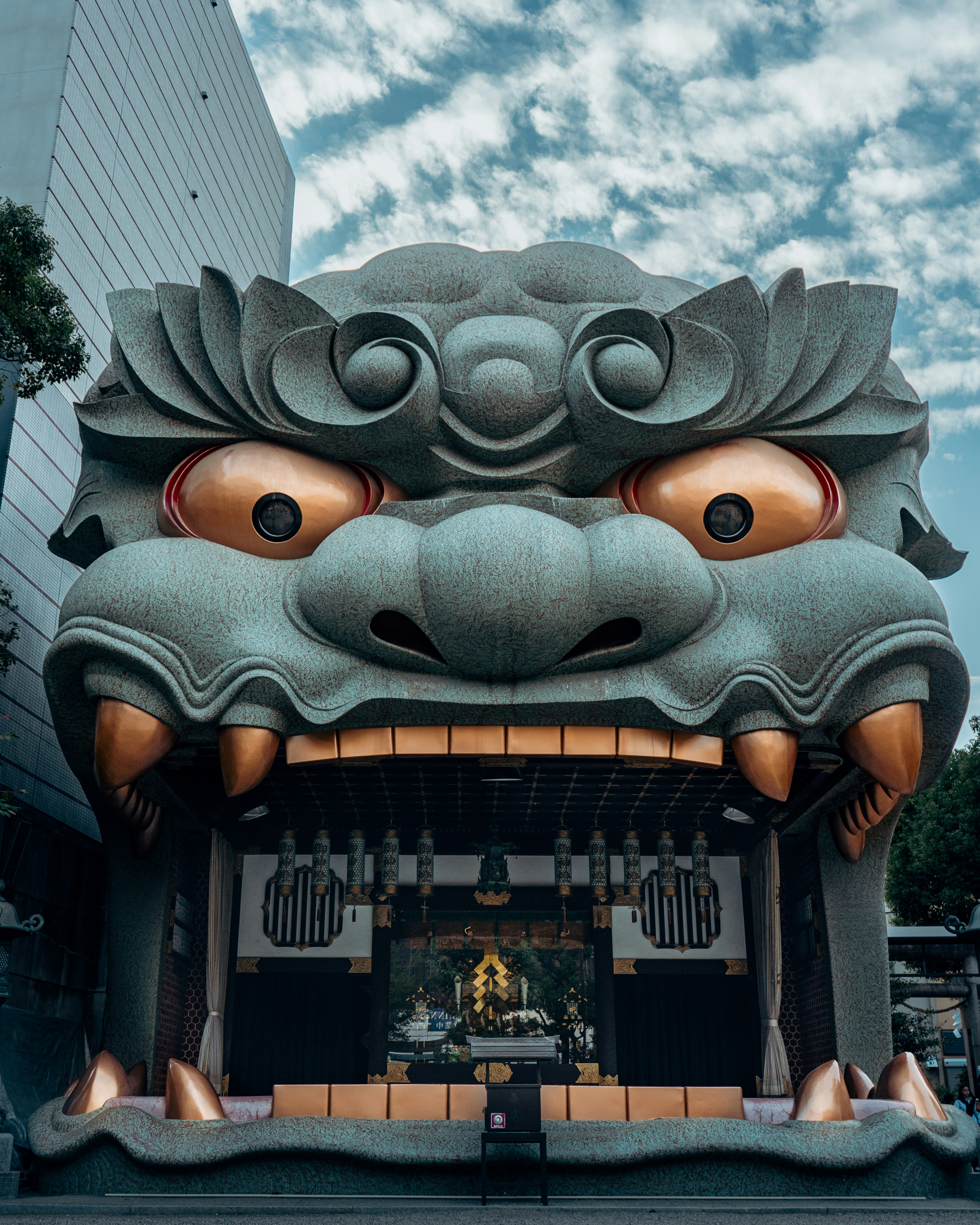 A dramatic front view of the giant lion-head stage at Namba Yasaka Shrine in Osaka, Japan, framed beneath a textured blue sky. The striking Shinto architecture, bronze details and monumental expression create one of Osaka’s most distinctive and photogenic cultural landmarks.