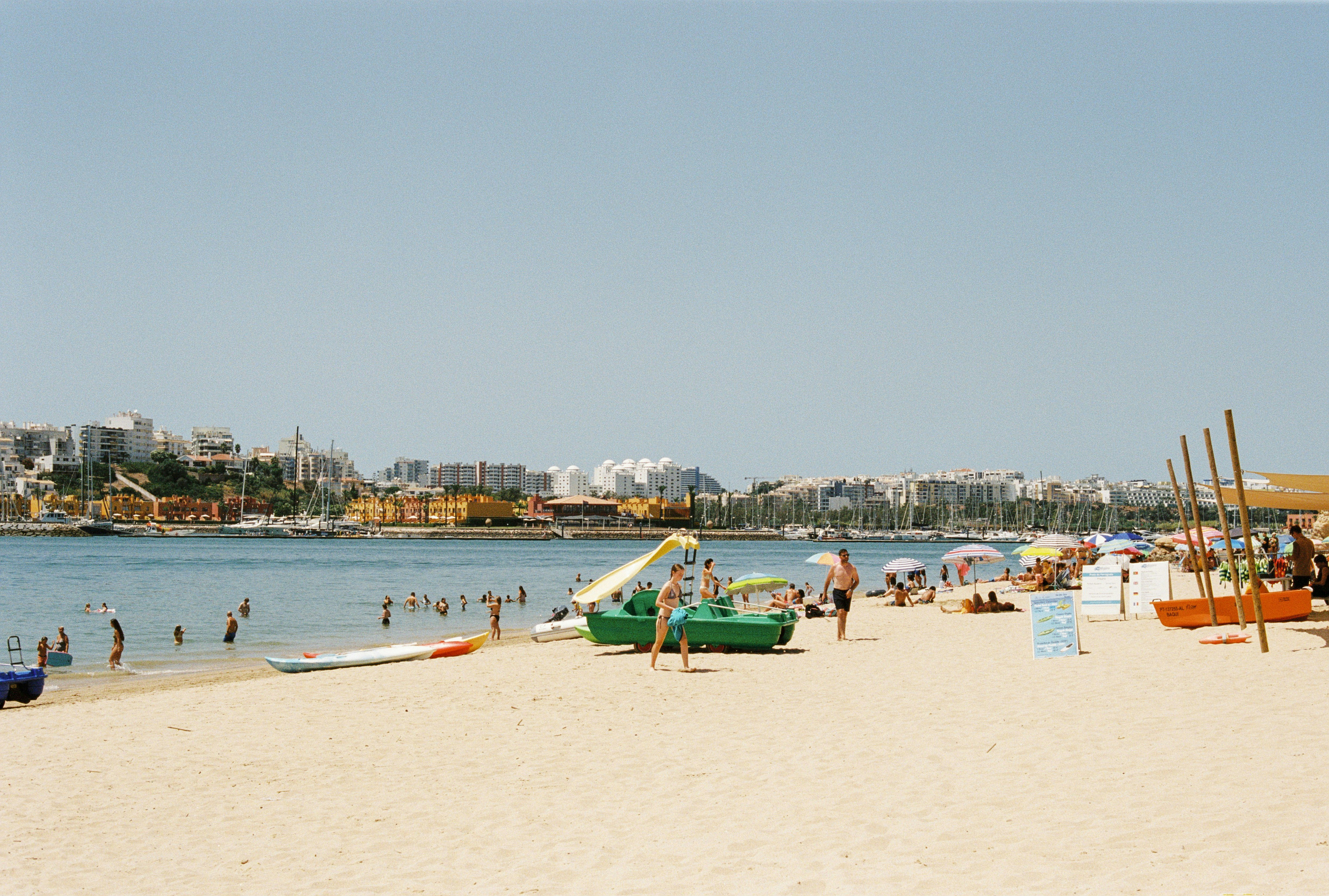 People on a sandy beach with pedal boats near a coastal town