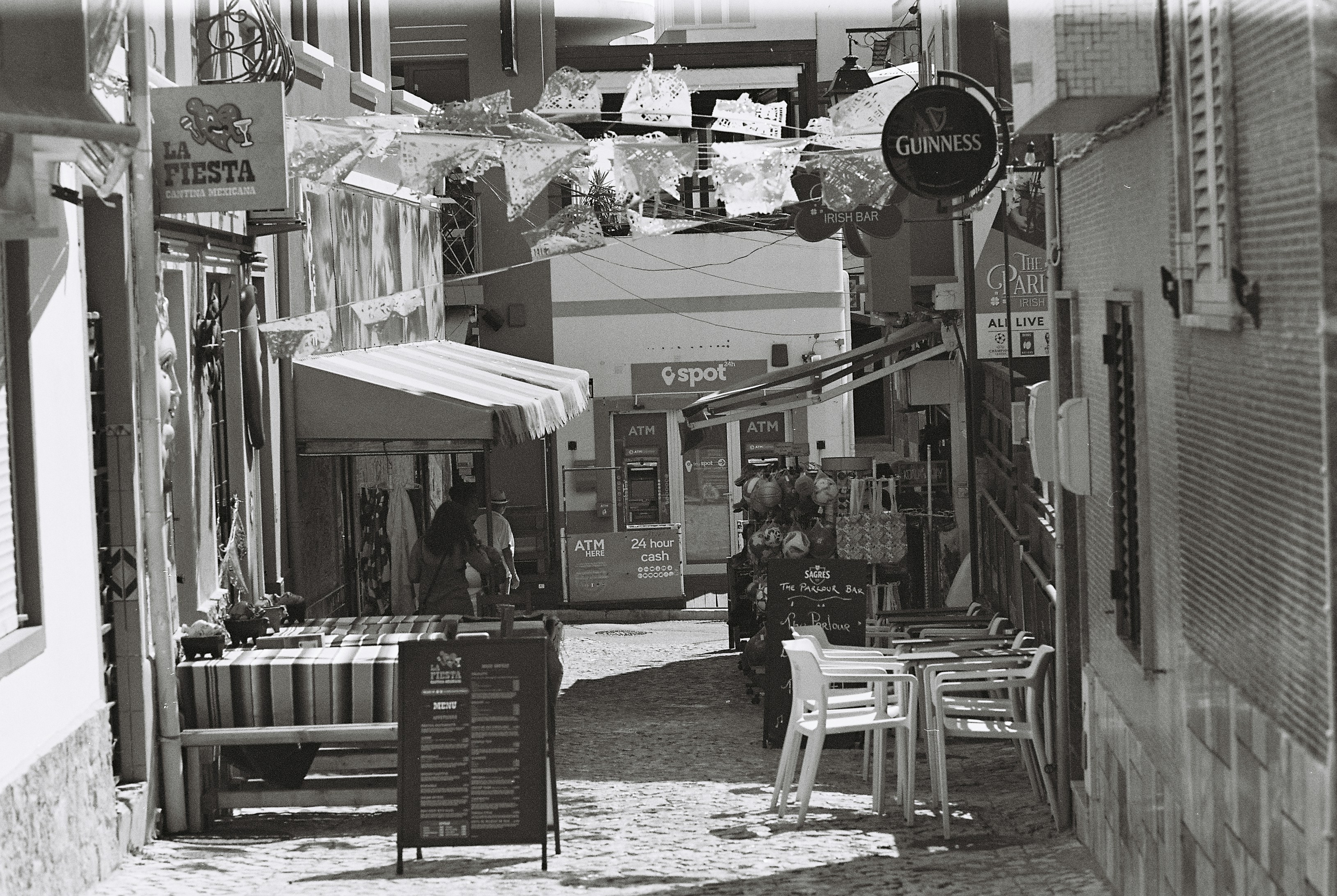 Bunting and bar signs hanging above a narrow cobbled street lined with cafes