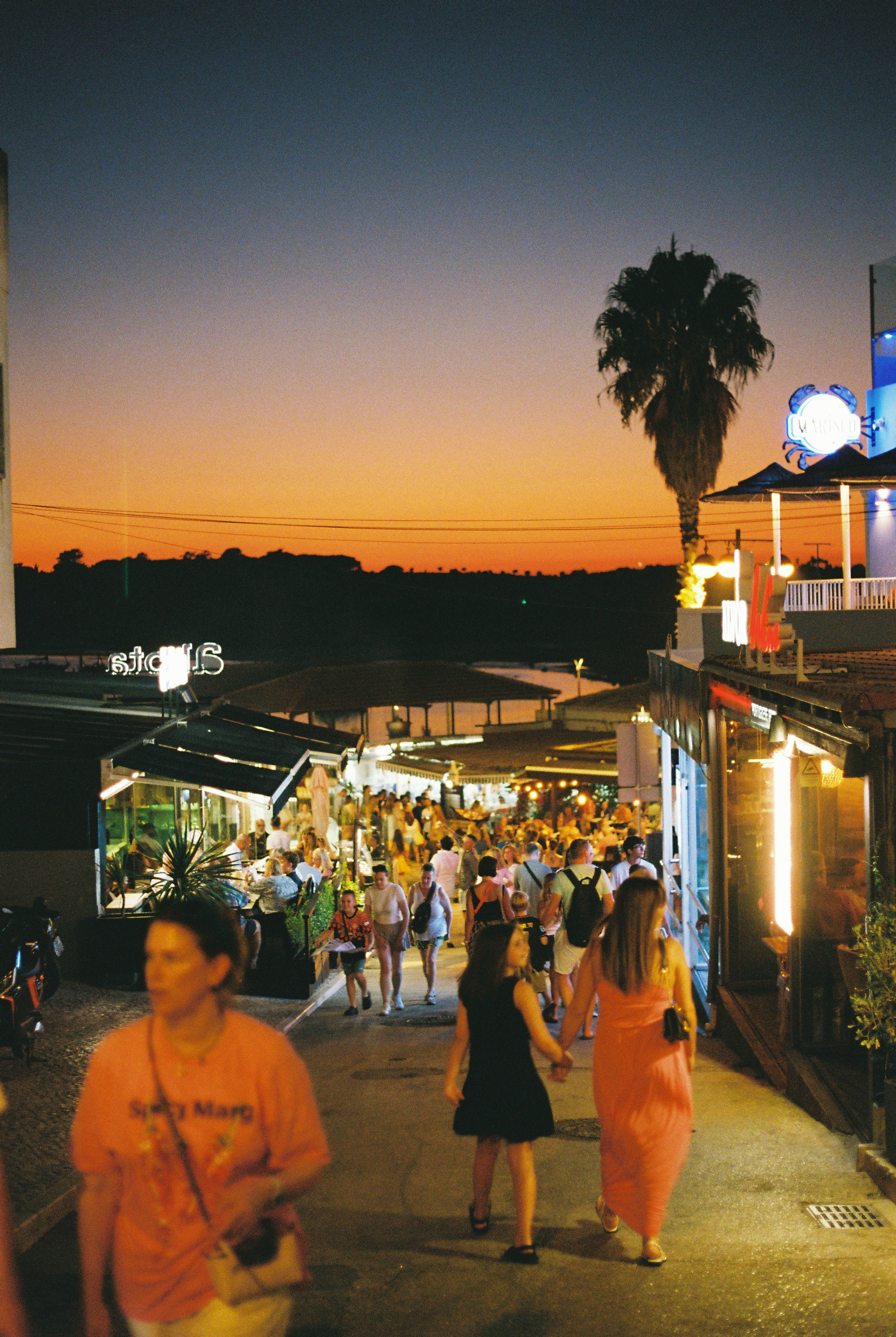 People walking along a street lined with restaurants during the golden hour