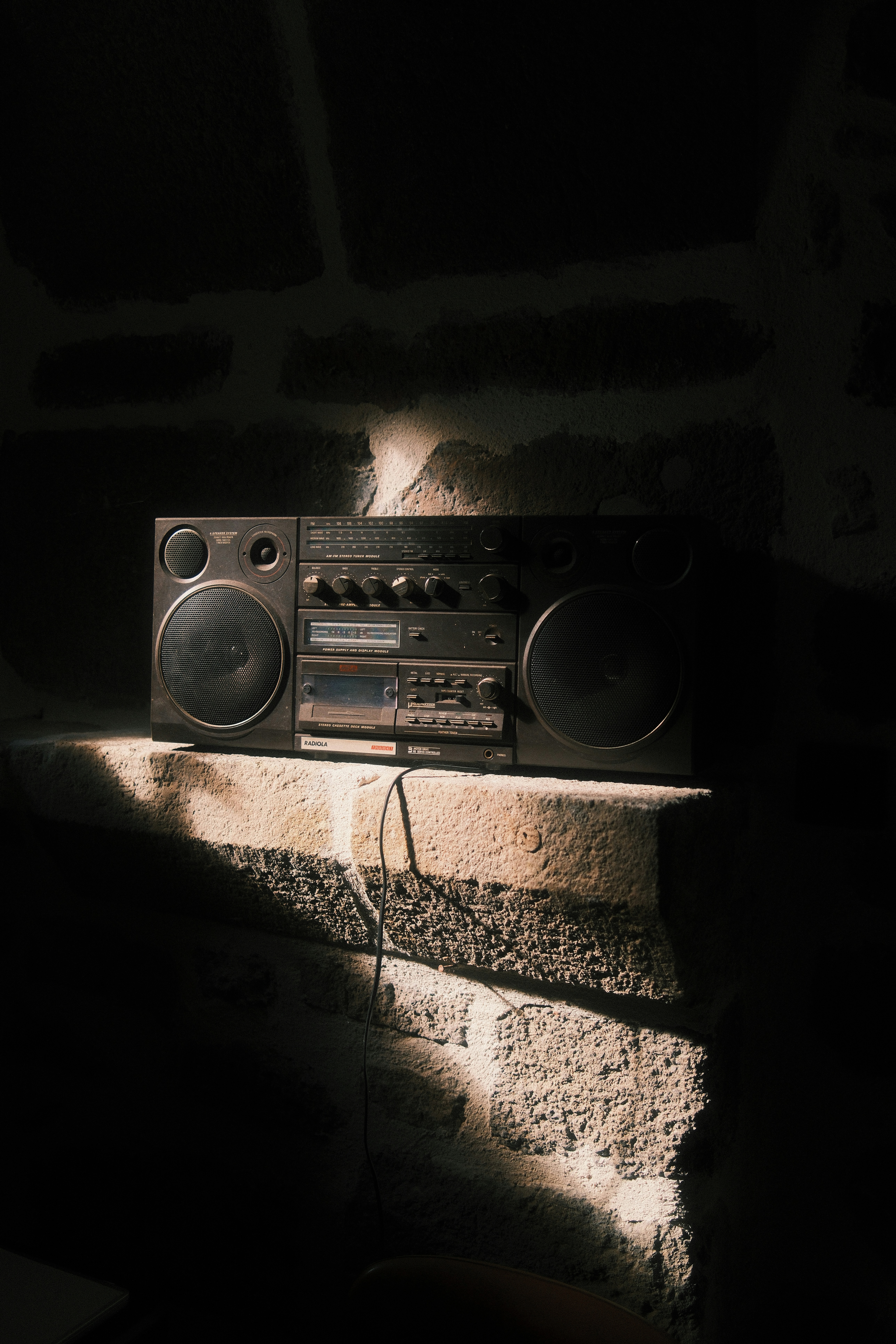 A vintage Radiola boombox on a rough stone ledge in dim light