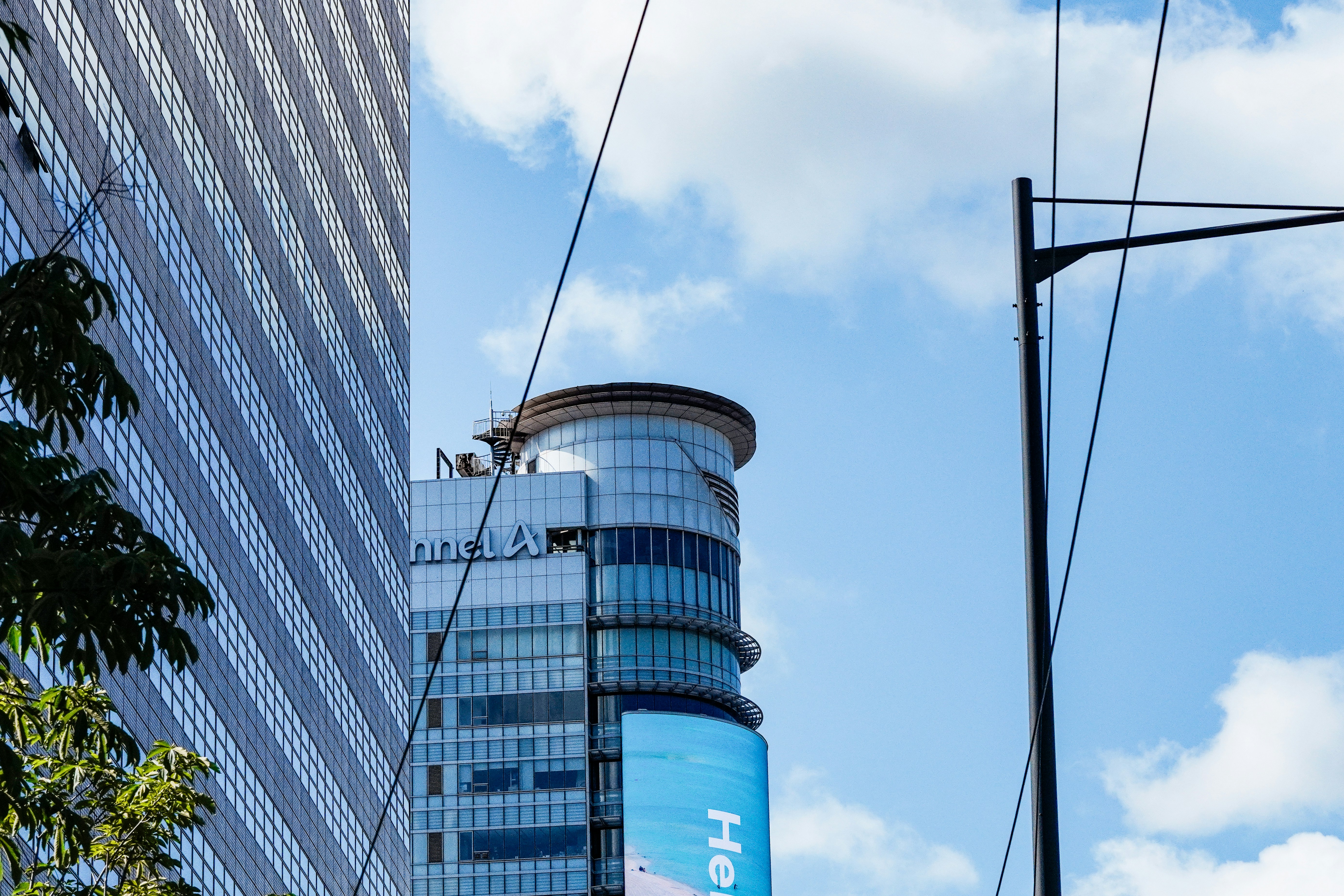 A modern glass skyscraper with a cylindrical top section against a blue sky
