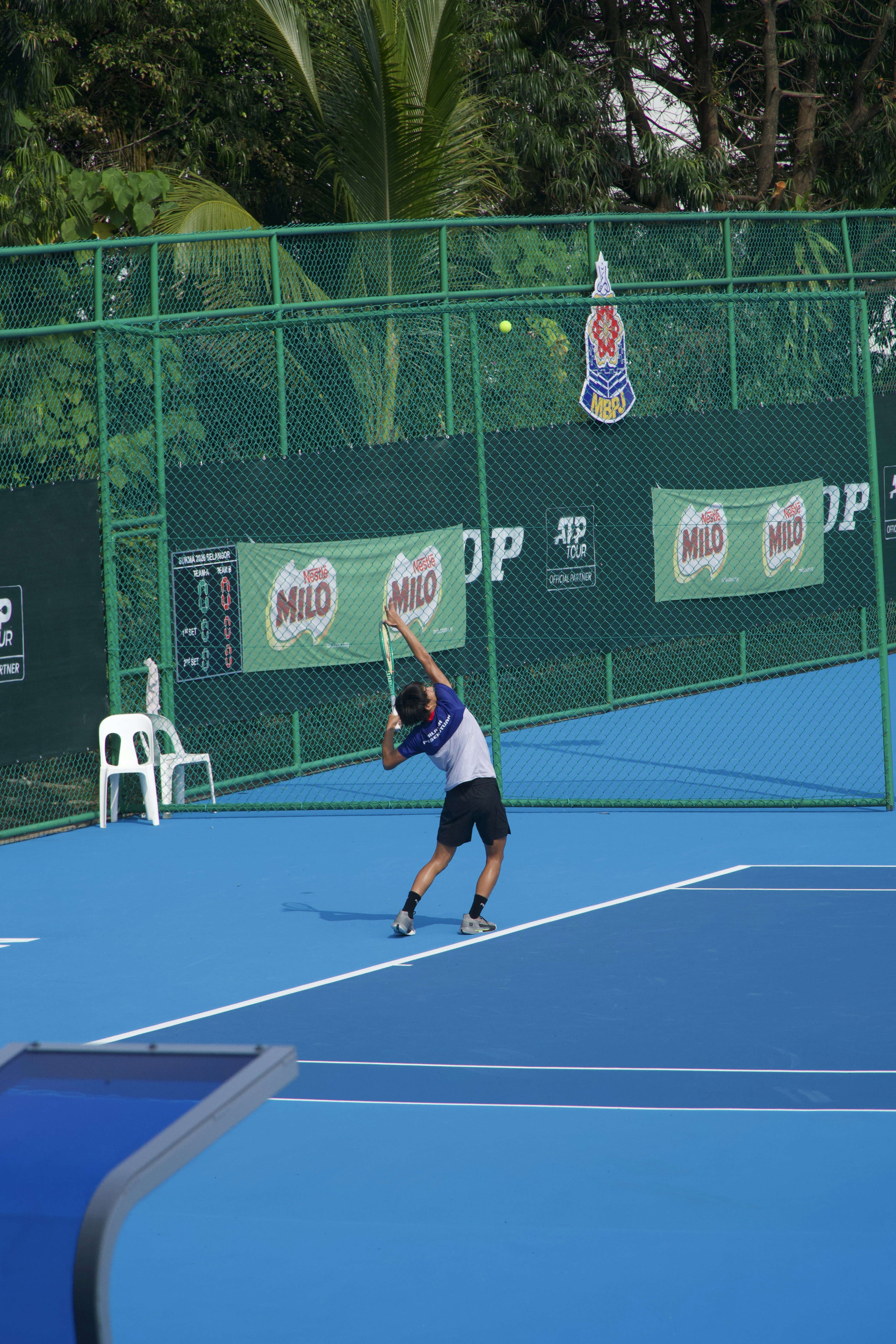A tennis player serving a ball on a bright blue outdoor court