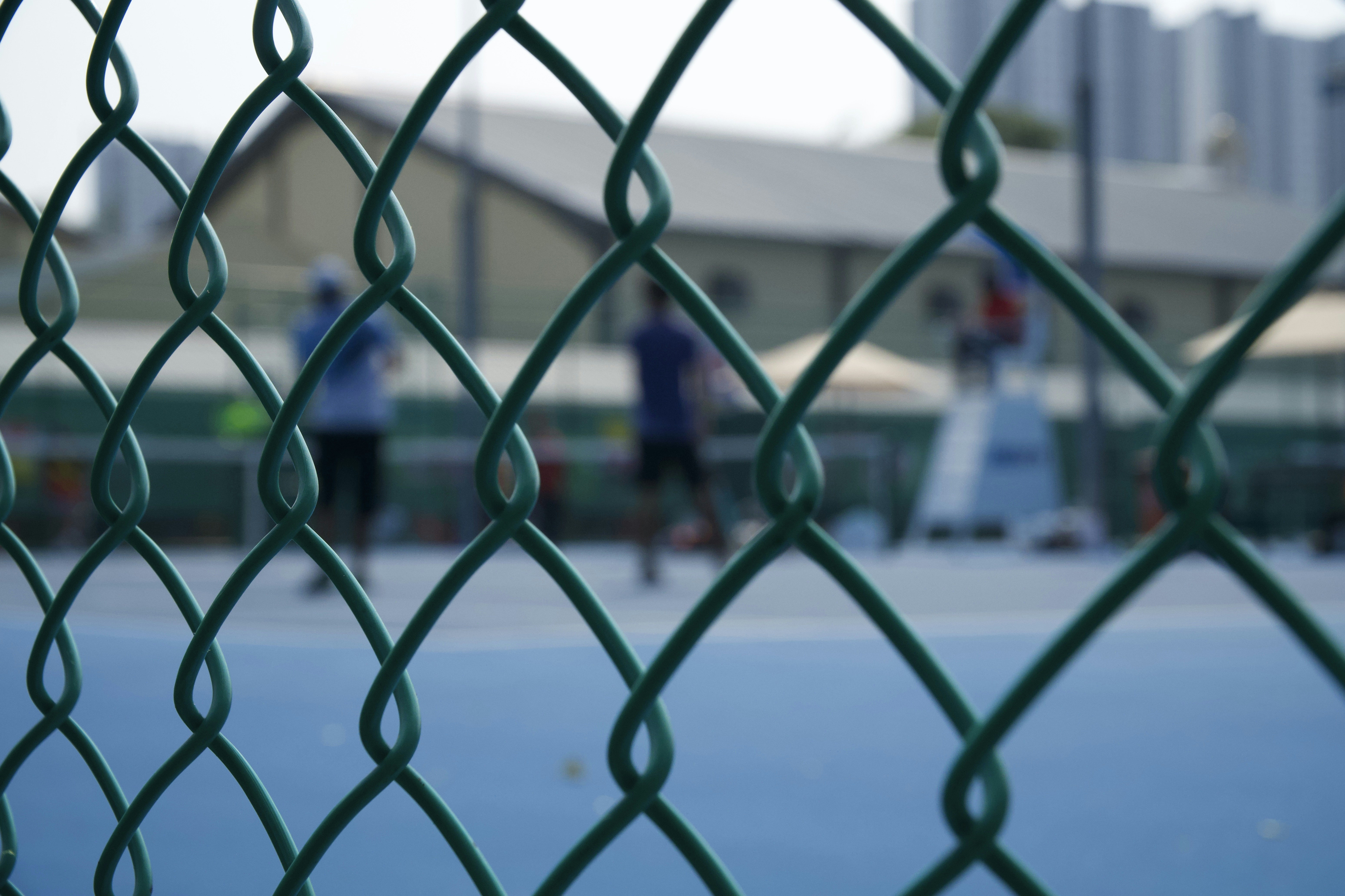 A green chain-link fence in front of people playing on a tennis court
