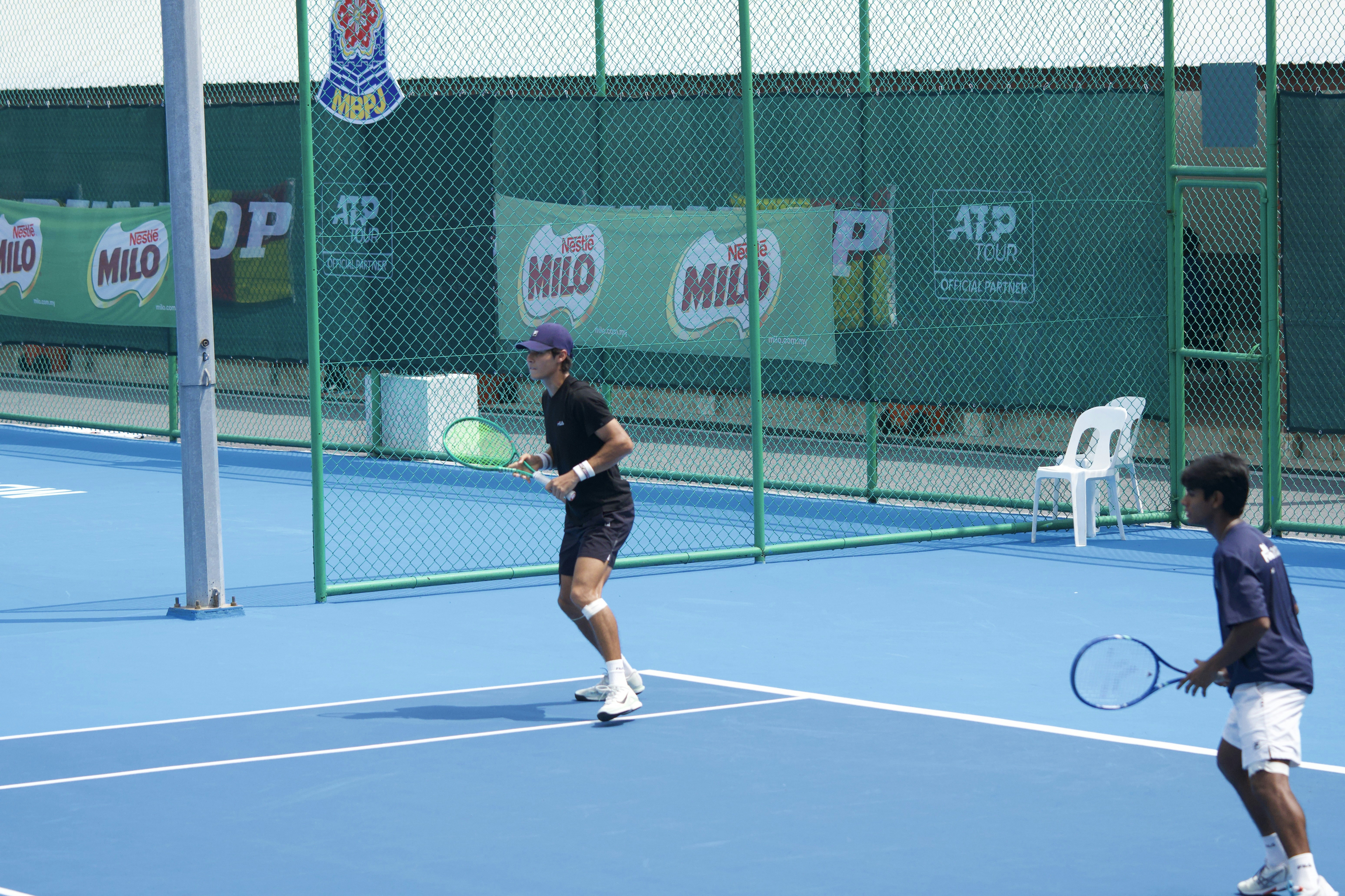Two people playing tennis on a blue court with green chain-link fencing