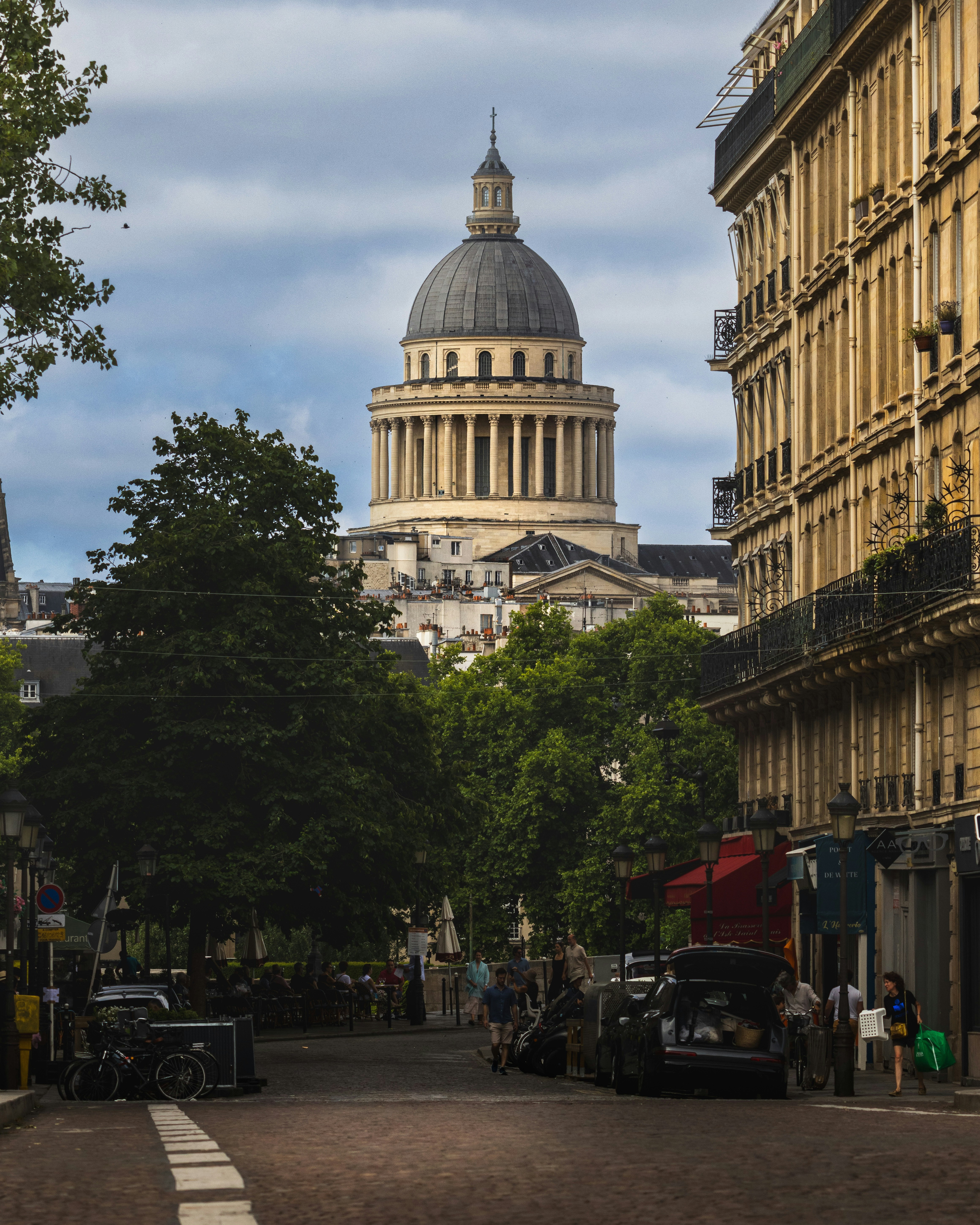 Die Pantheon-Kuppel erhebt sich über einer baumgesäumten Straße in Paris mit Fußgängern