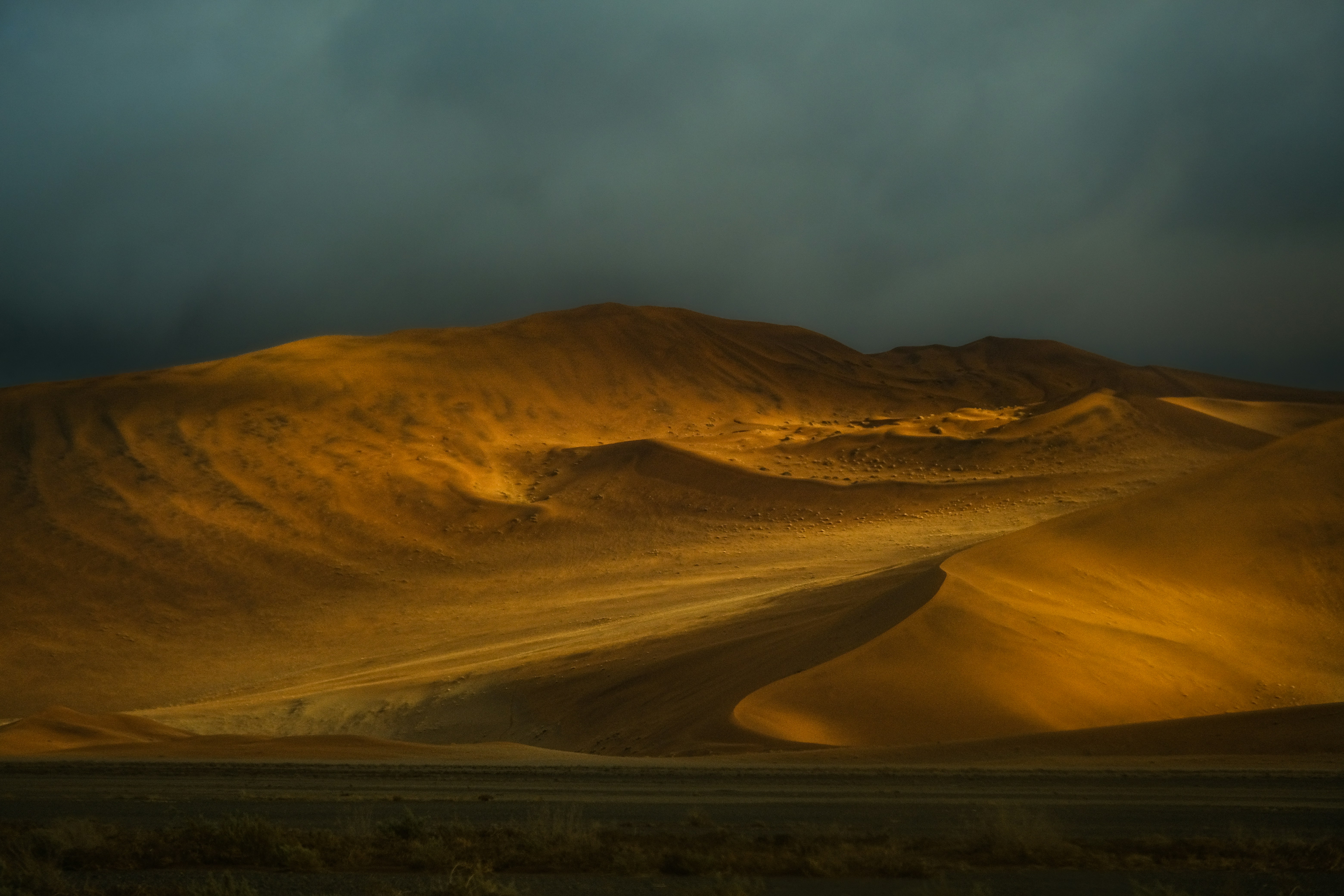 Golden sand dunes under a dark and stormy sky in the desert