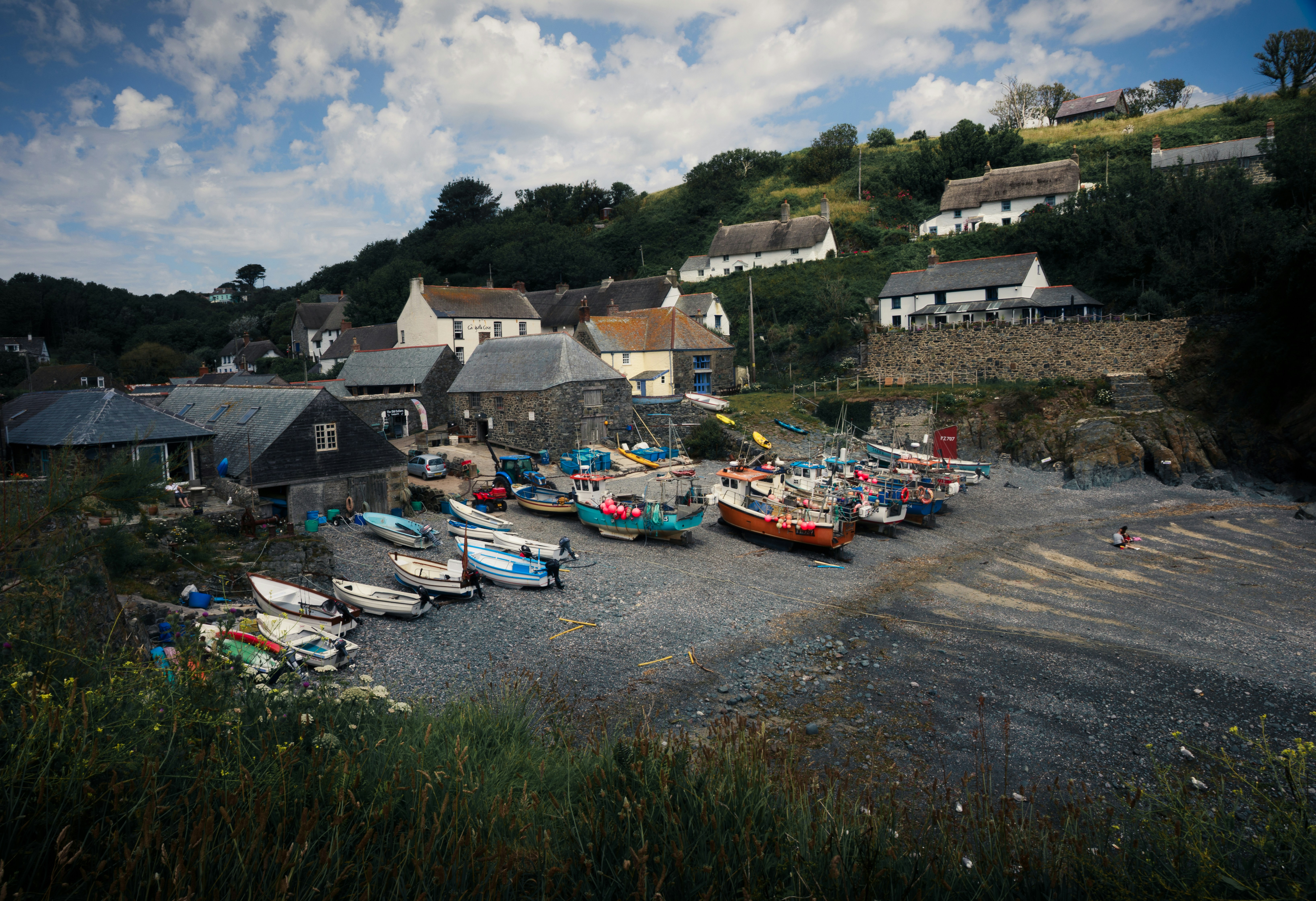 Fishing boats on a pebble beach below a village with stone cottages