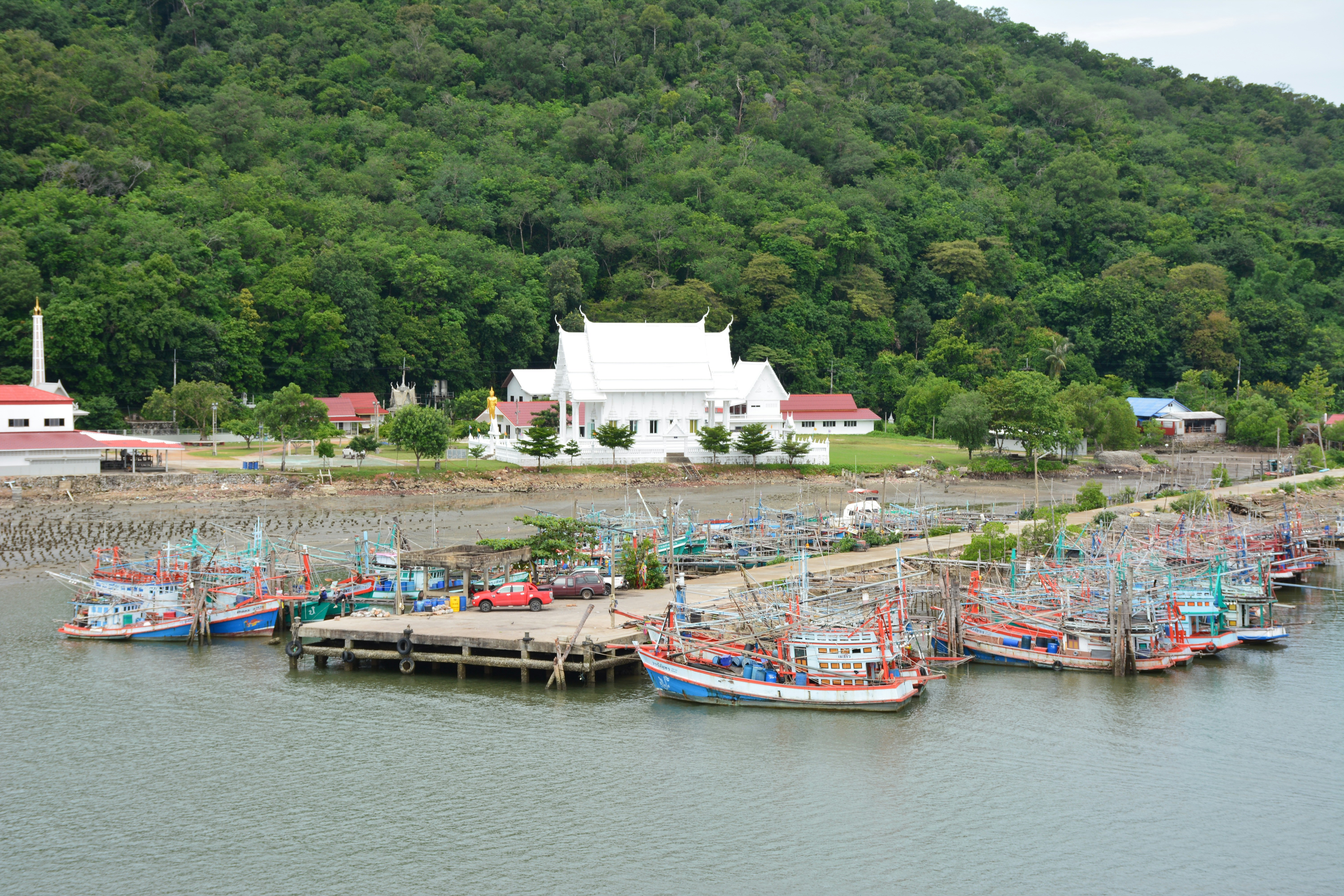 Colourful wooden fishing boats moored at a pier below a white temple and green hills