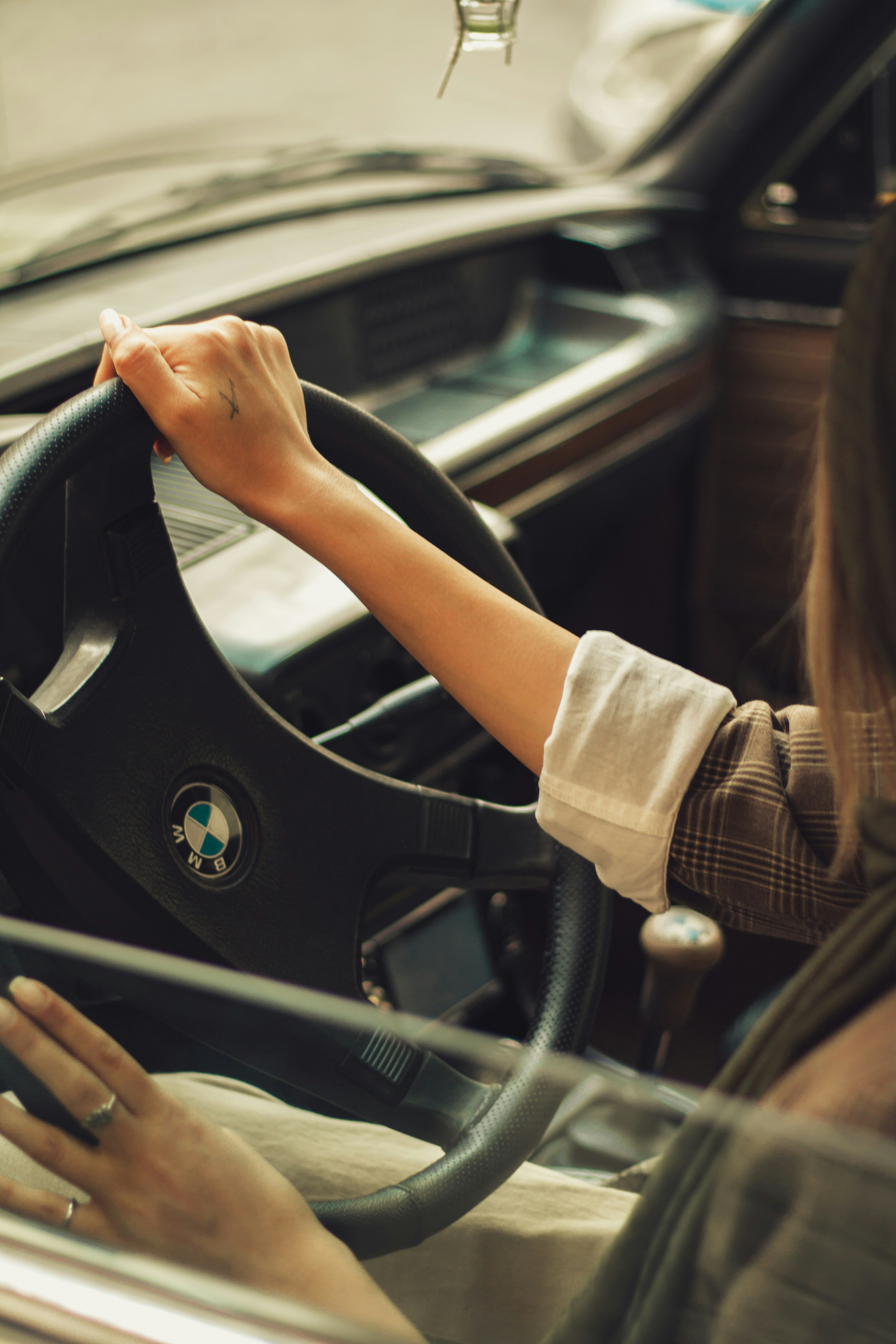 A person driving a vintage BMW with hands on the steering wheel