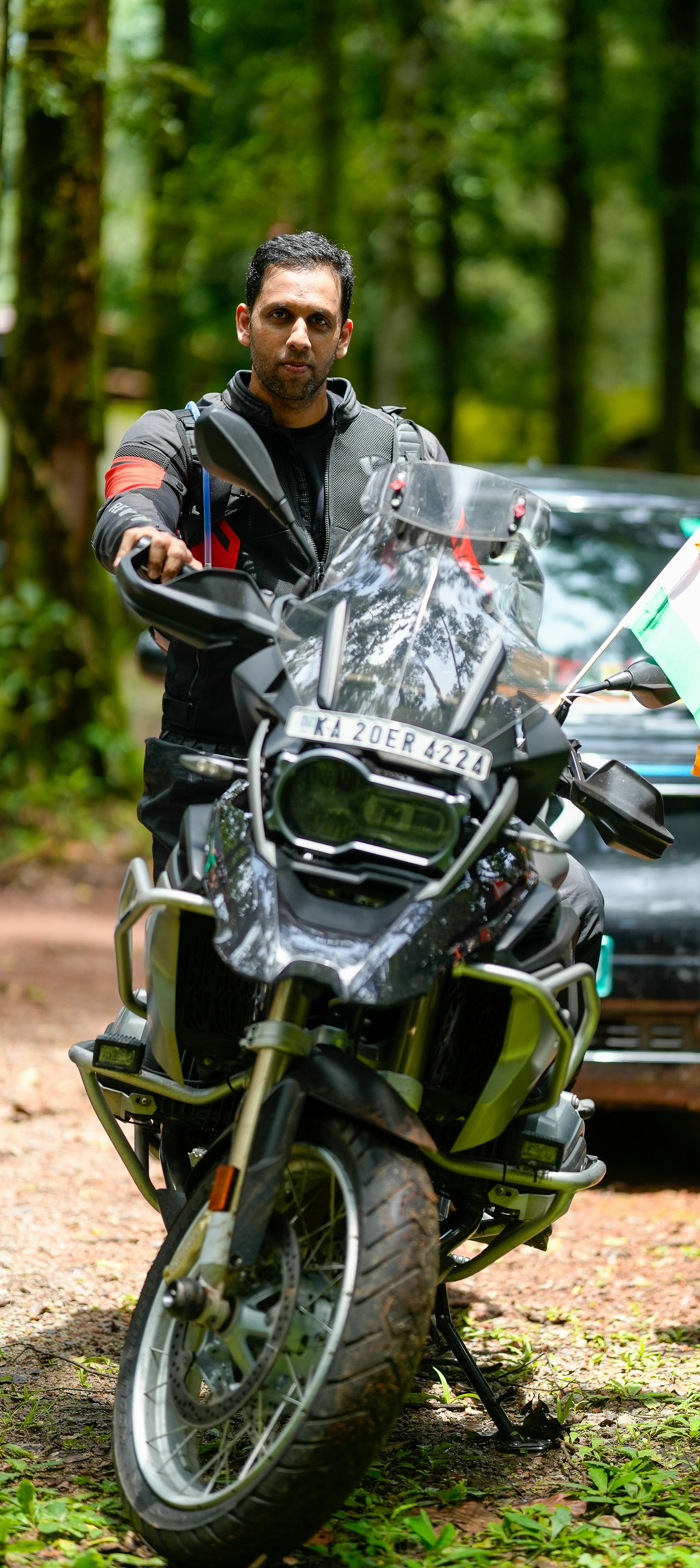 A man in a black motorcycle jacket on a large adventure motorcycle in a forest