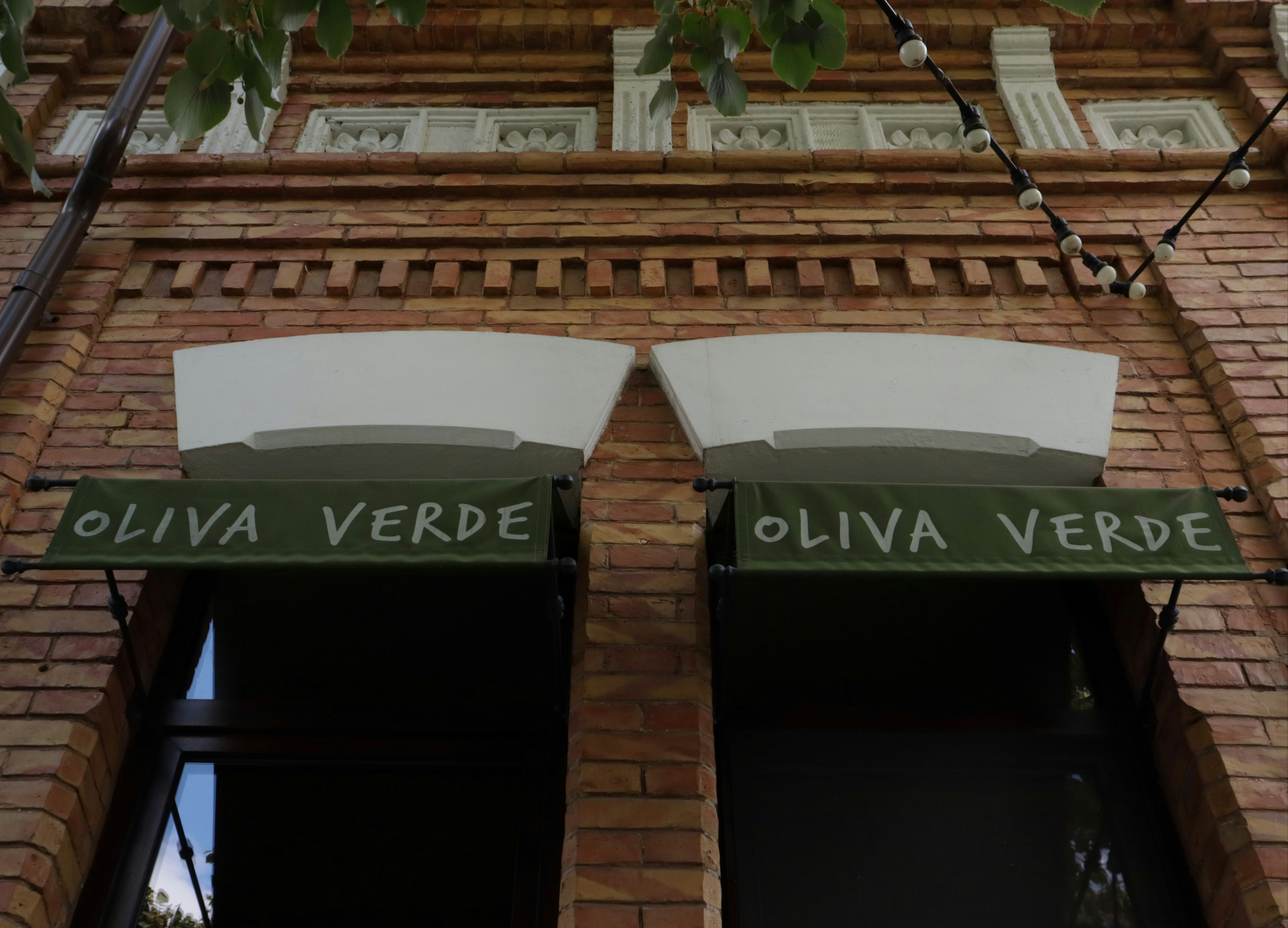 Two green awnings reading "OLIVA VERDE" above windows on a brick building facade